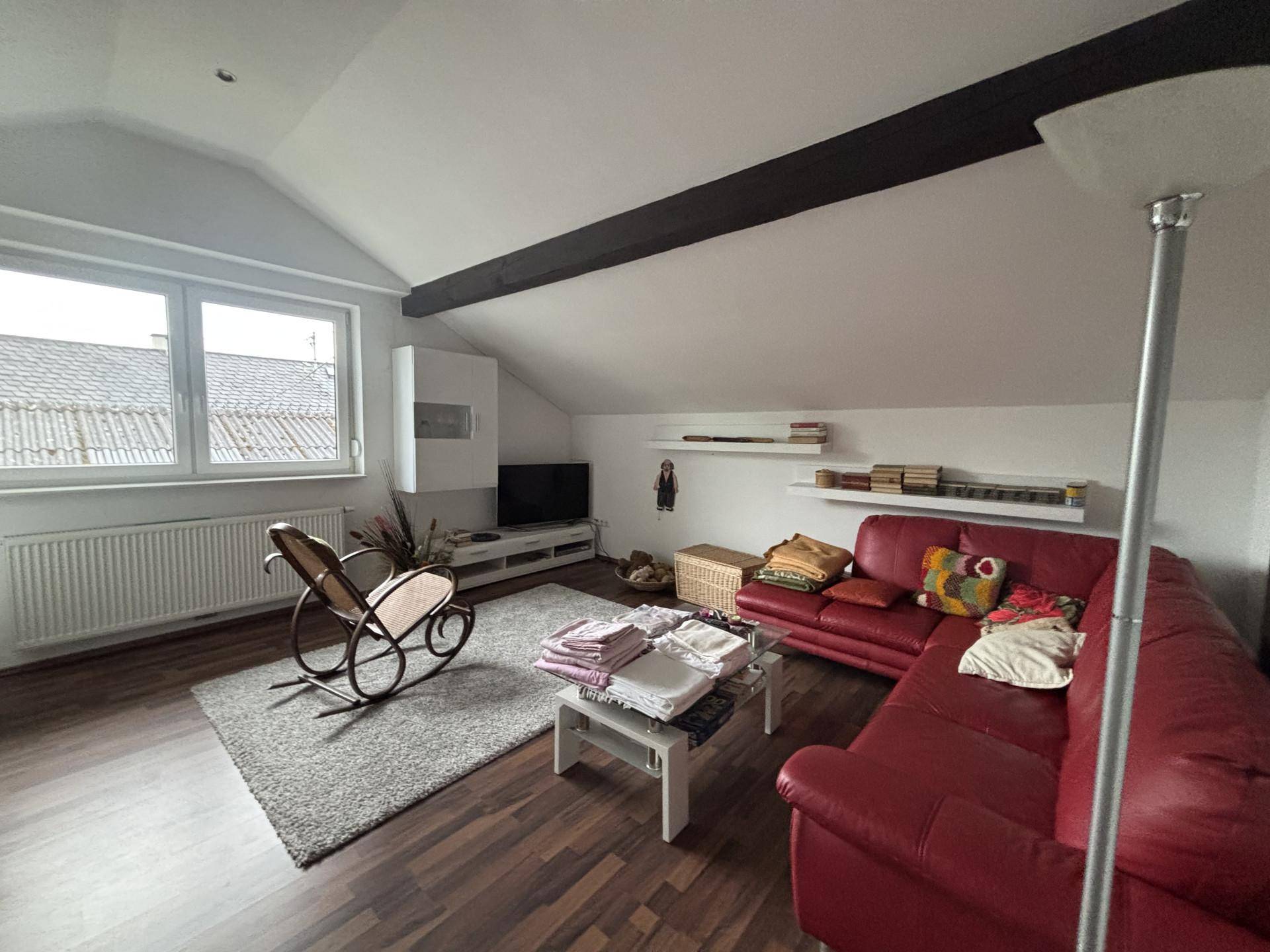 Gemütliches Wohnzimmer im Dachgeschoss mit rotem Sofa, Holzbalken und Laminatboden.