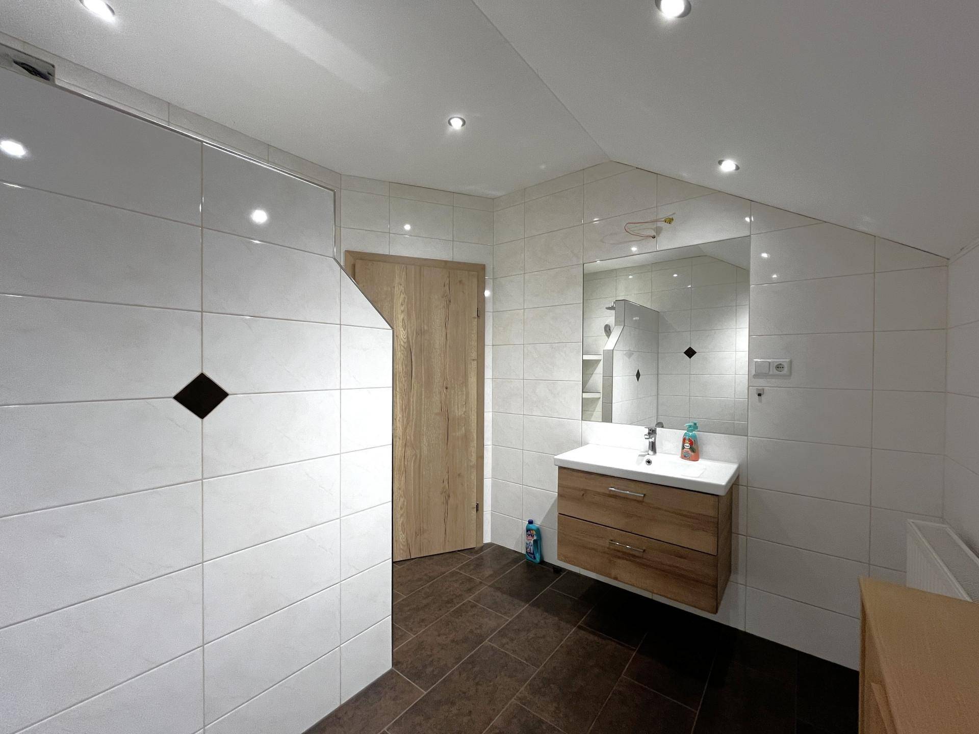 Modern gefliestes Badezimmer mit Holzwaschtisch und Spiegelschrank unter einer Dachschräge.