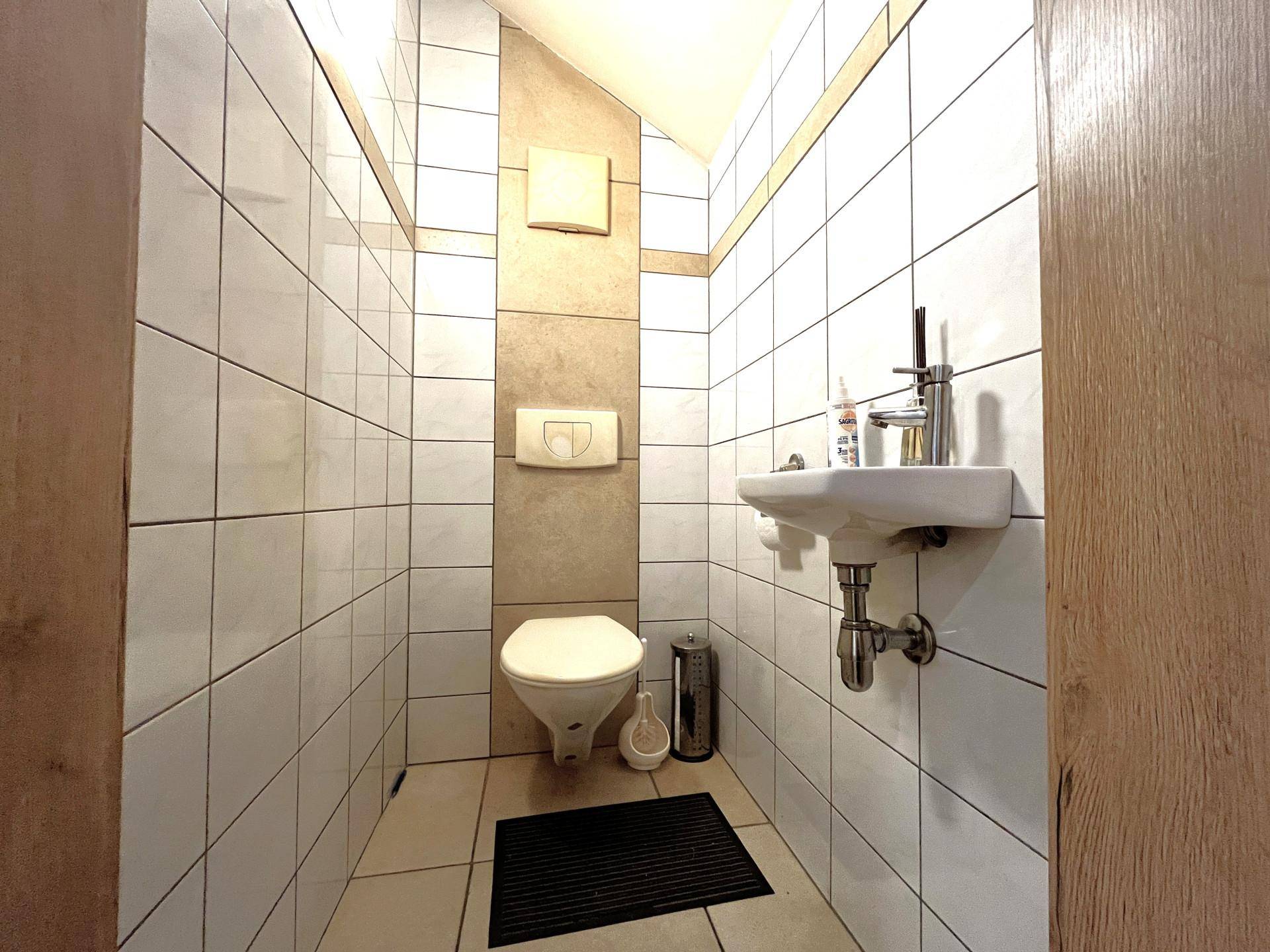 Kleines Gäste-WC mit weißen Fliesen, wandhängendem WC und Handwaschbecken, funktional und sauber.