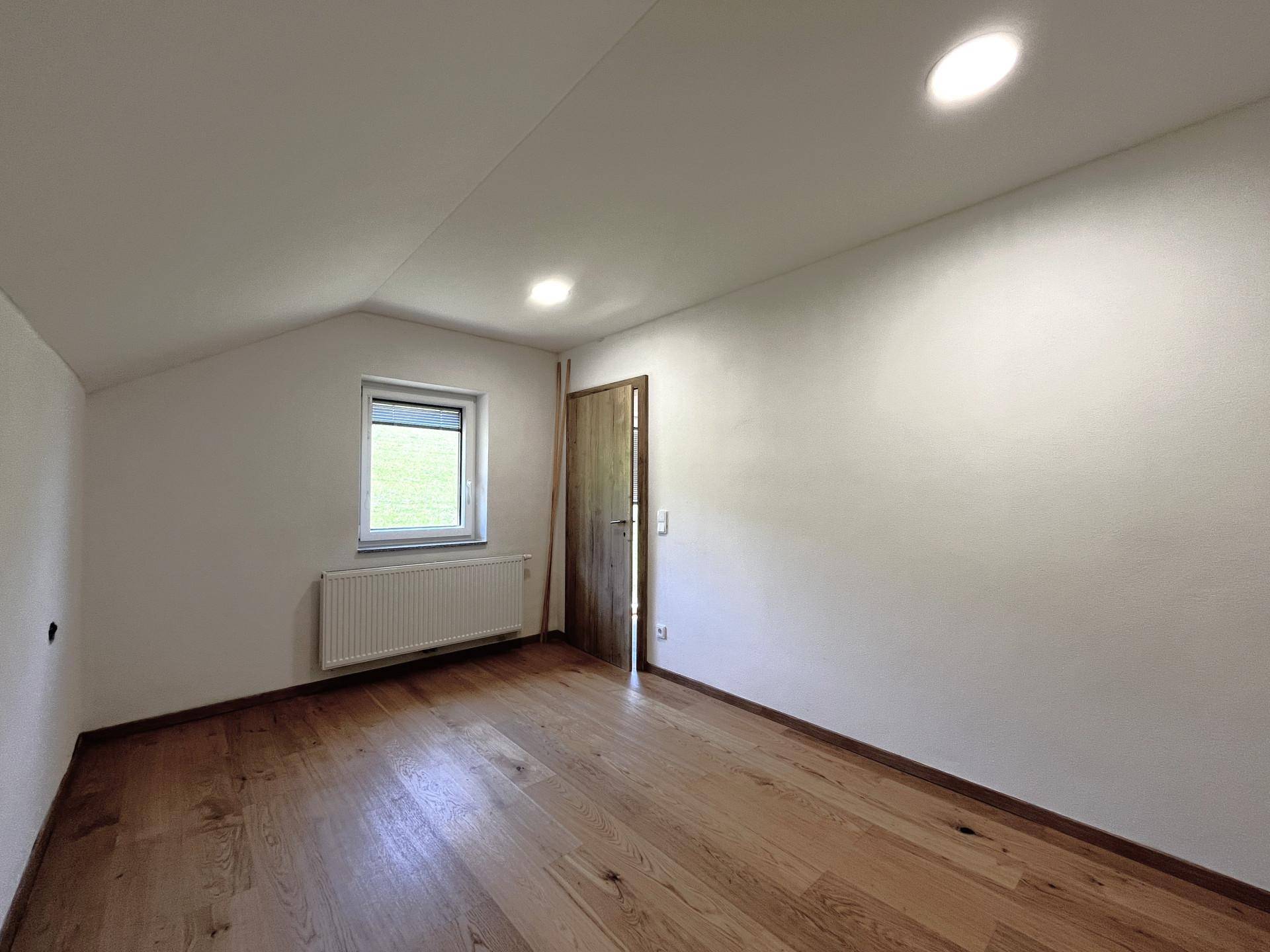 Helles Zimmer mit Holzboden, Fenster und Dachschräge, ideal als Schlaf- oder Arbeitszimmer.