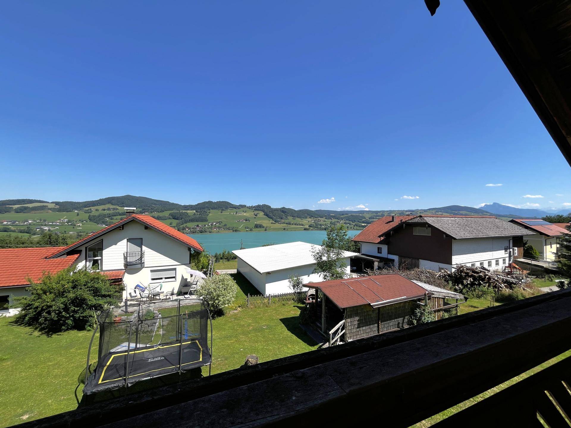 Balkon mit weitem Blick auf den See, die grüne Landschaft und ein Trampolin im Garten.