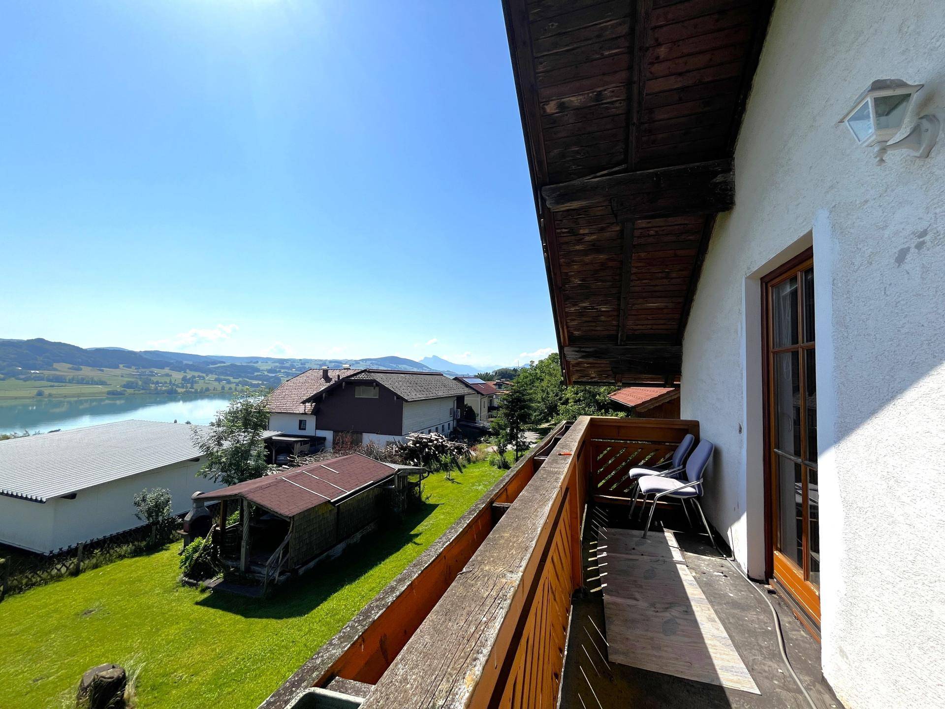 Langer Holzbalkon mit Sitzgelegenheiten und Panoramablick auf die umliegende Natur und den See.