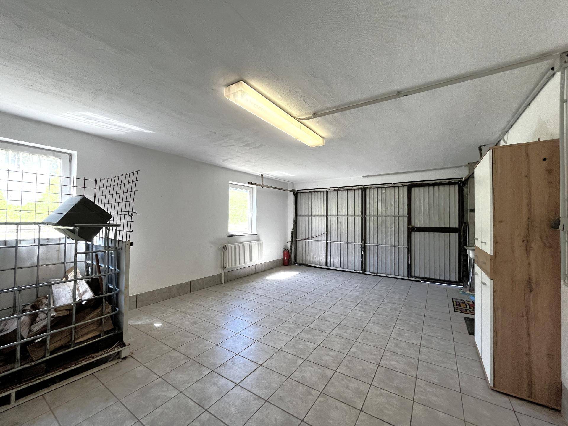 Geräumige Garage mit Fliesenboden, Fenstern und Stauraum, hell beleuchtet und funktional.