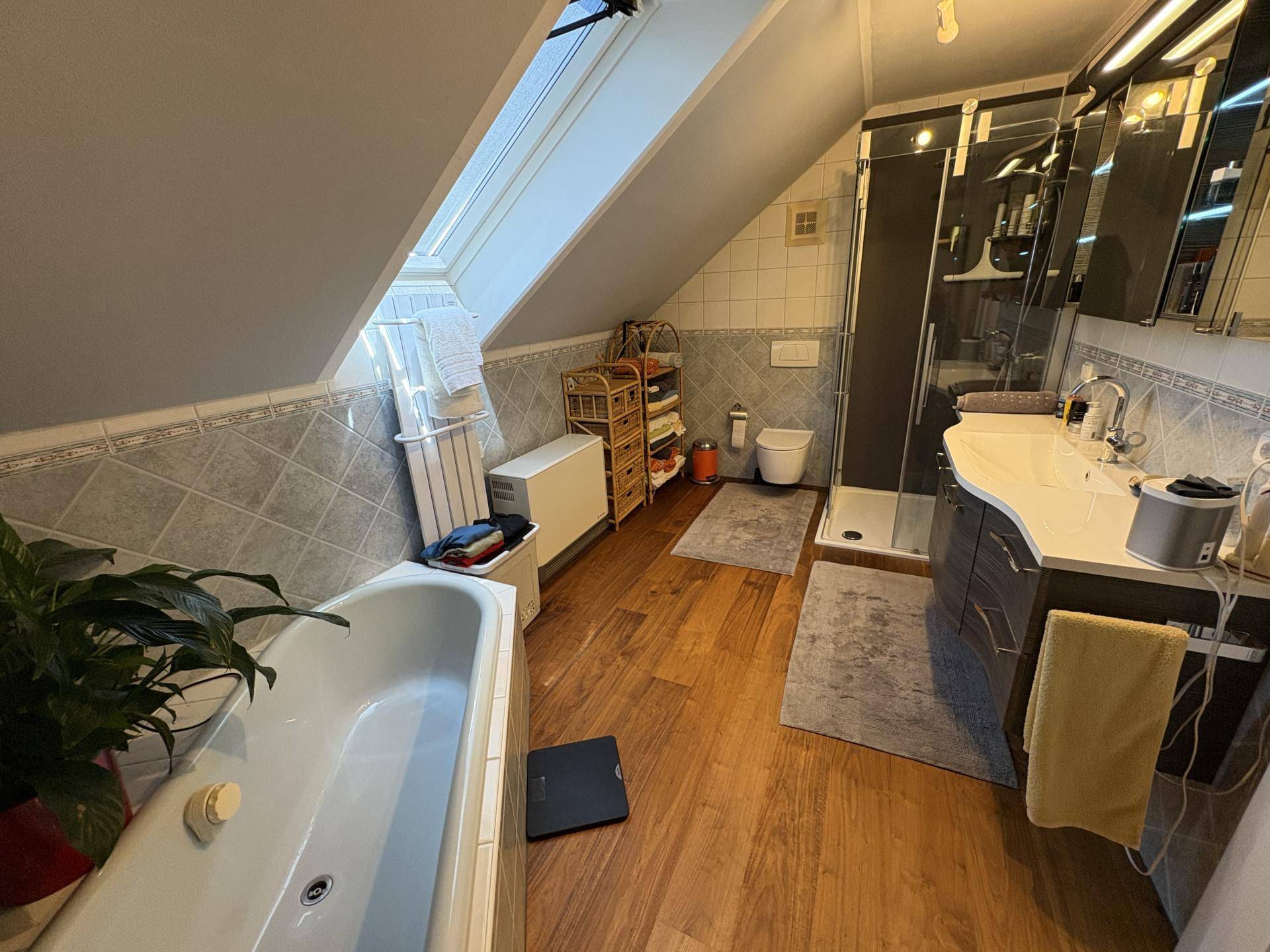 Badezimmer mit Badewanne, Duschkabine, Waschtisch und Dachfenster unter einer Dachschräge.