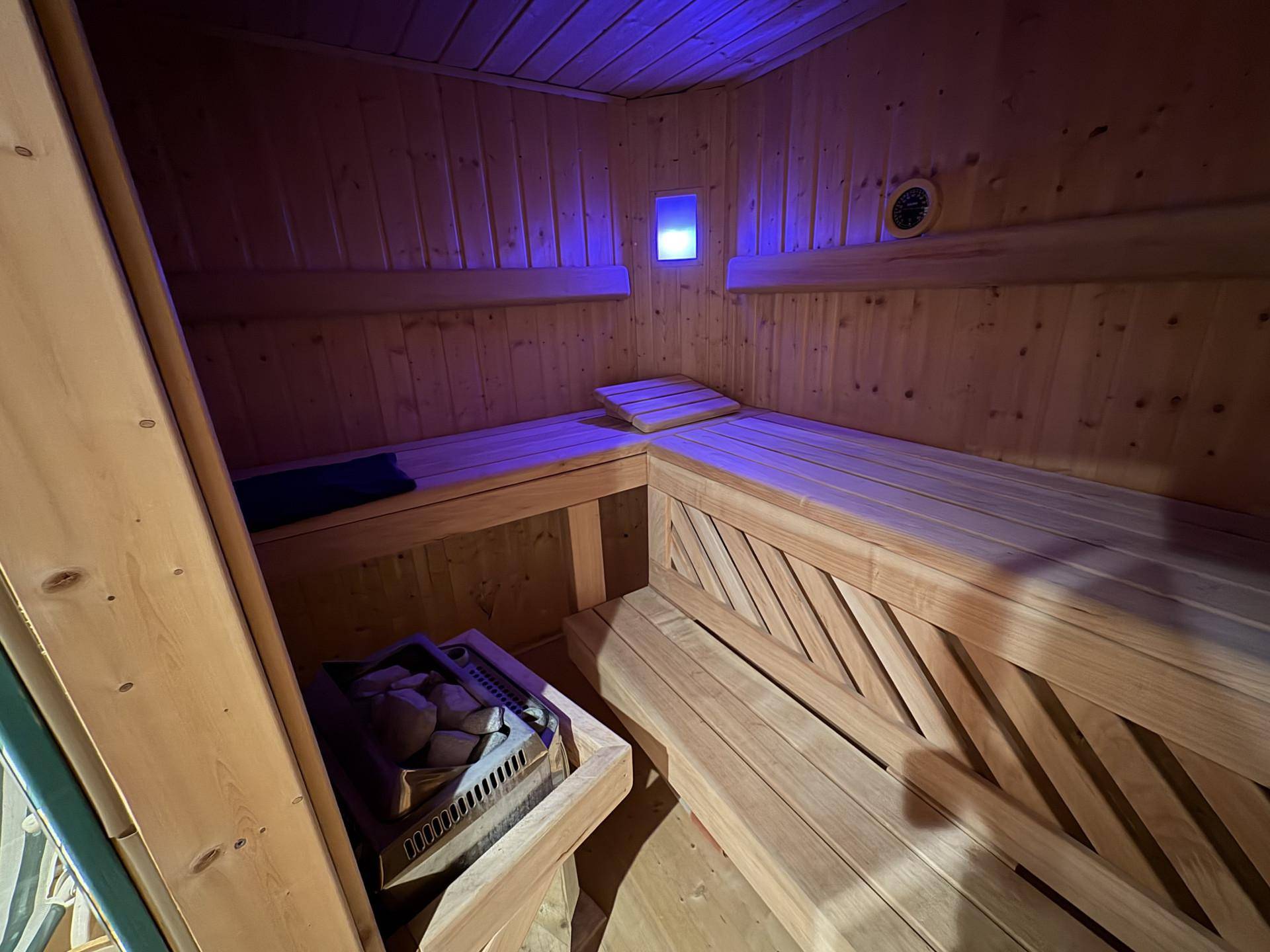Holzsauna mit Sitzbänken und Ofen, stimmungsvoll beleuchtet für Entspannung und Wellness.
