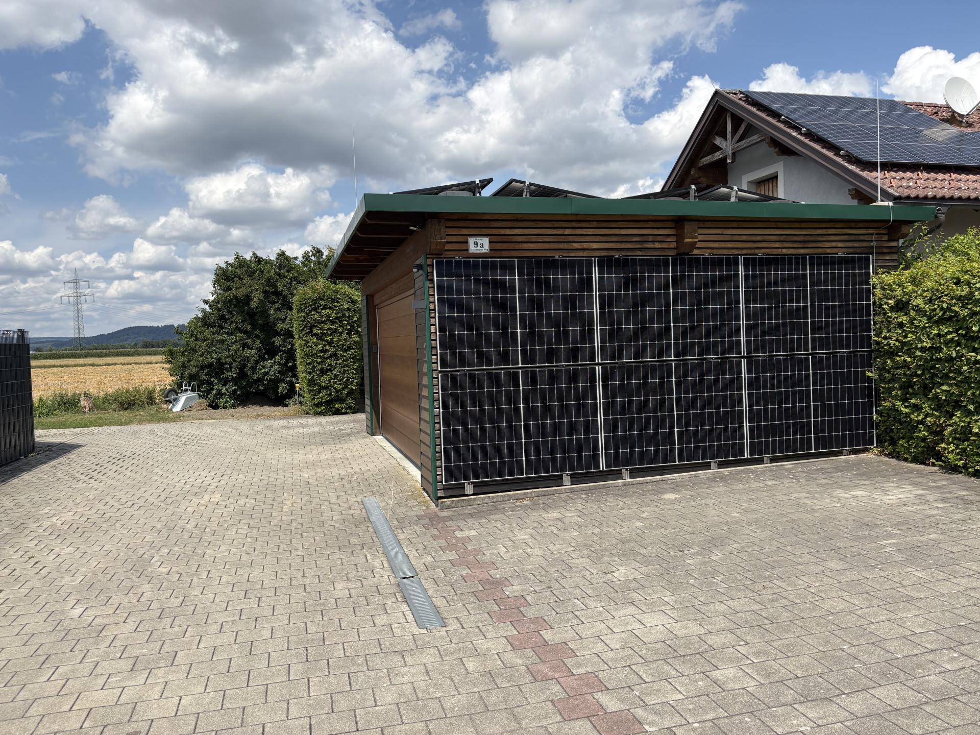 Garage mit Solarpaneelen an der Seite und auf dem Dach, davor eine gepflasterte Zufahrt.