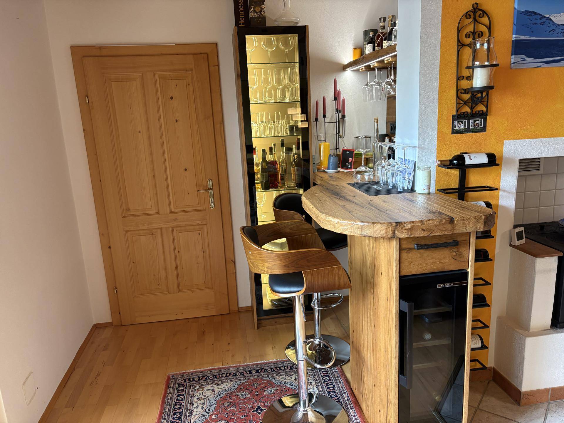 Rustikale Bar mit Holztresen, Barhockern, Weinkühler und beleuchteter Vitrine.
