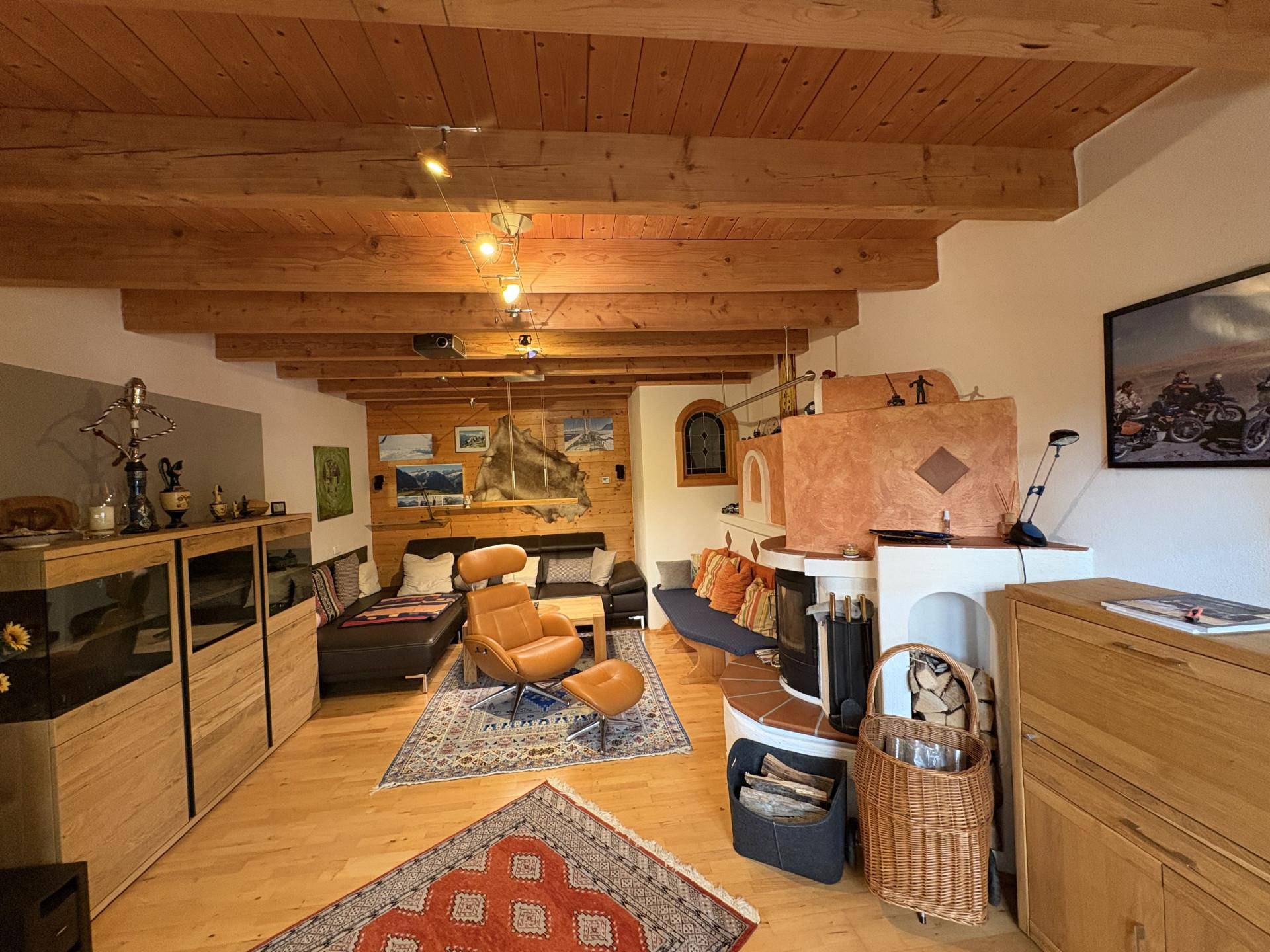 Gemütliches Wohnzimmer mit sichtbaren Holzbalken, einem traditionellen Kachelofen und Parkettboden.