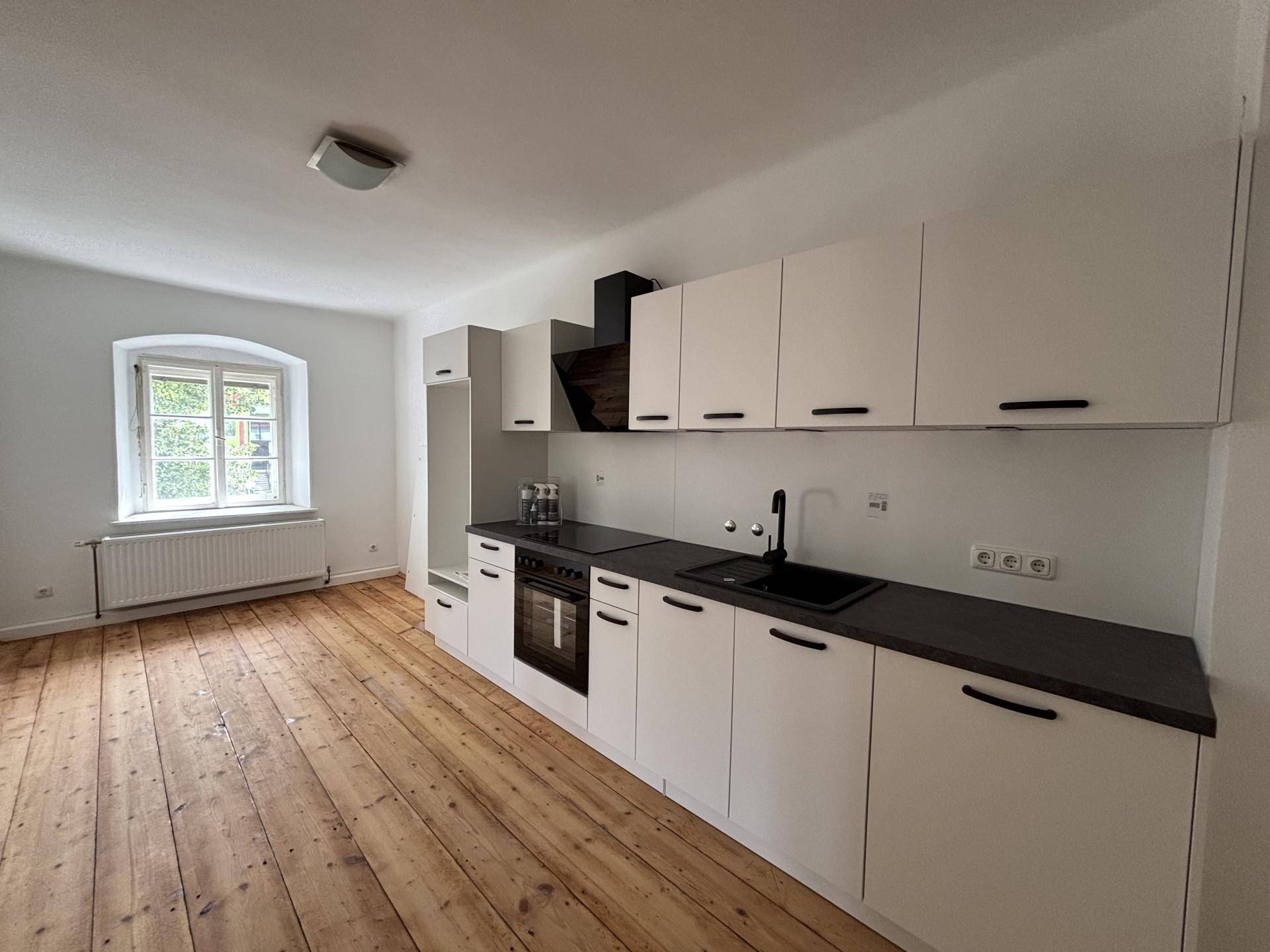 Moderne, helle Küche mit weißen Schränken, dunkler Arbeitsplatte und Holzplankenboden.