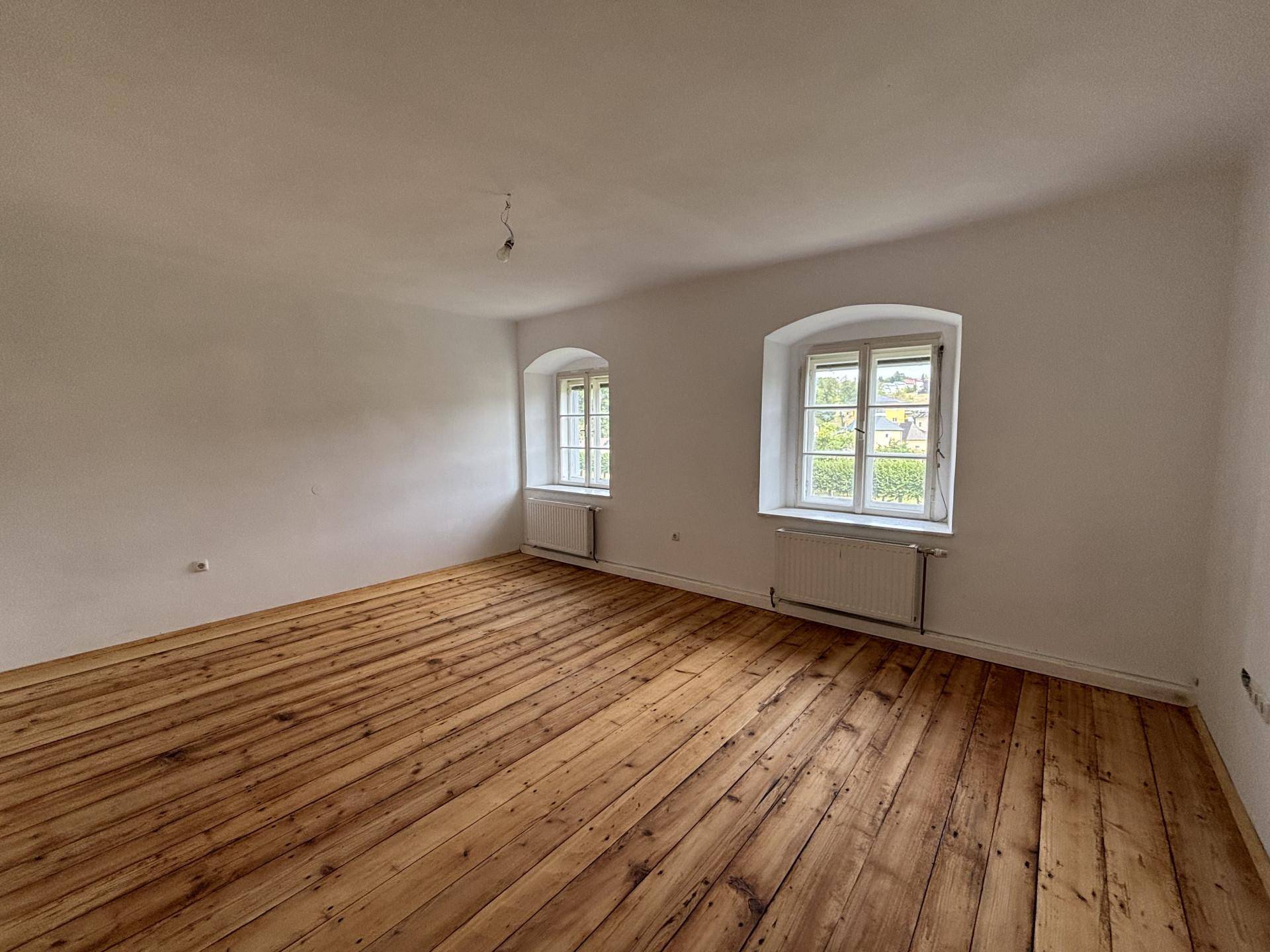 Geräumiges, helles Zimmer mit Holzdielenboden und zwei Fenstern mit Blick ins Grüne.
