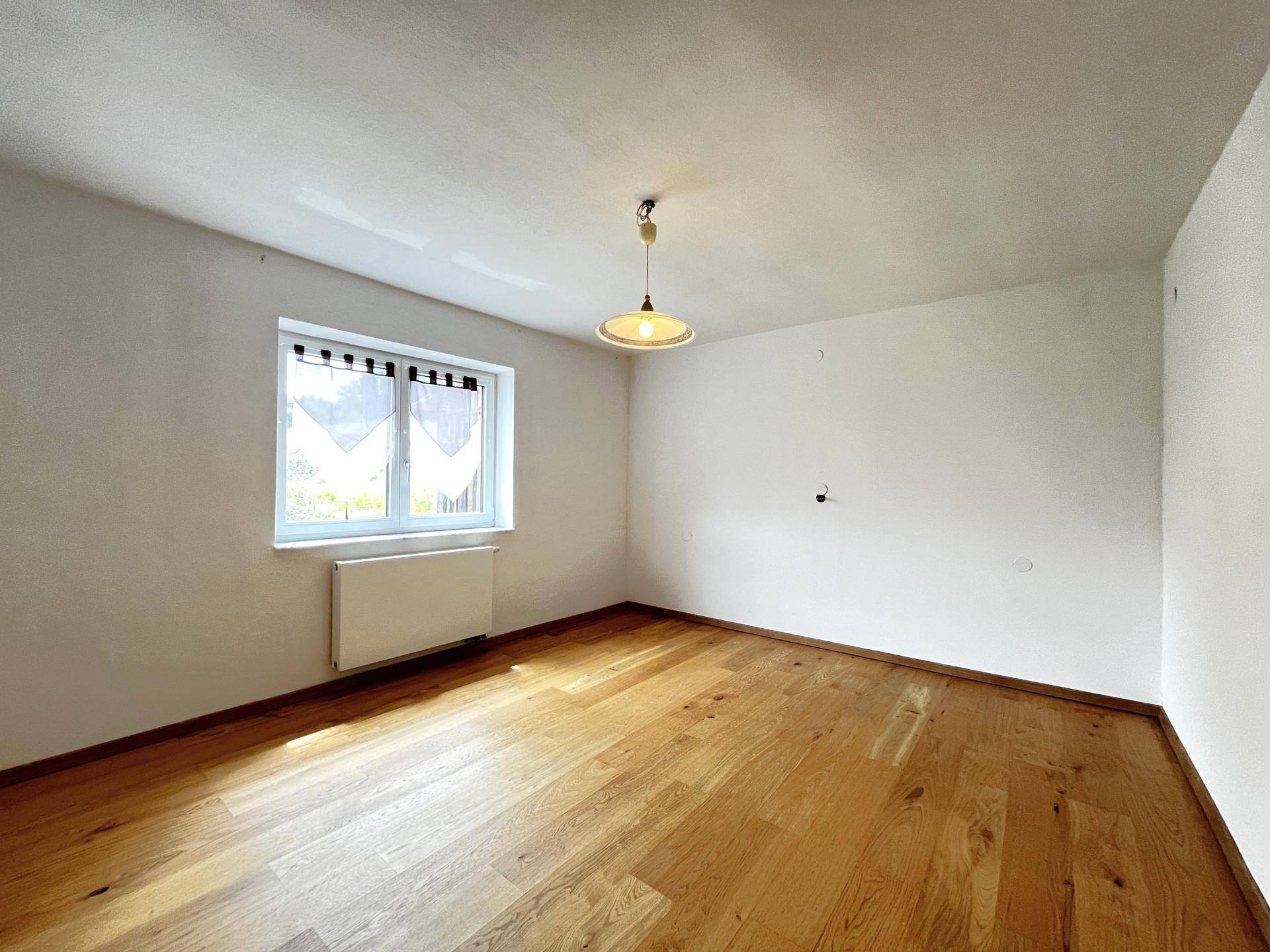 Helles Schlafzimmer mit Holzboden und einem Fenster, bereit zur individuellen Gestaltung.