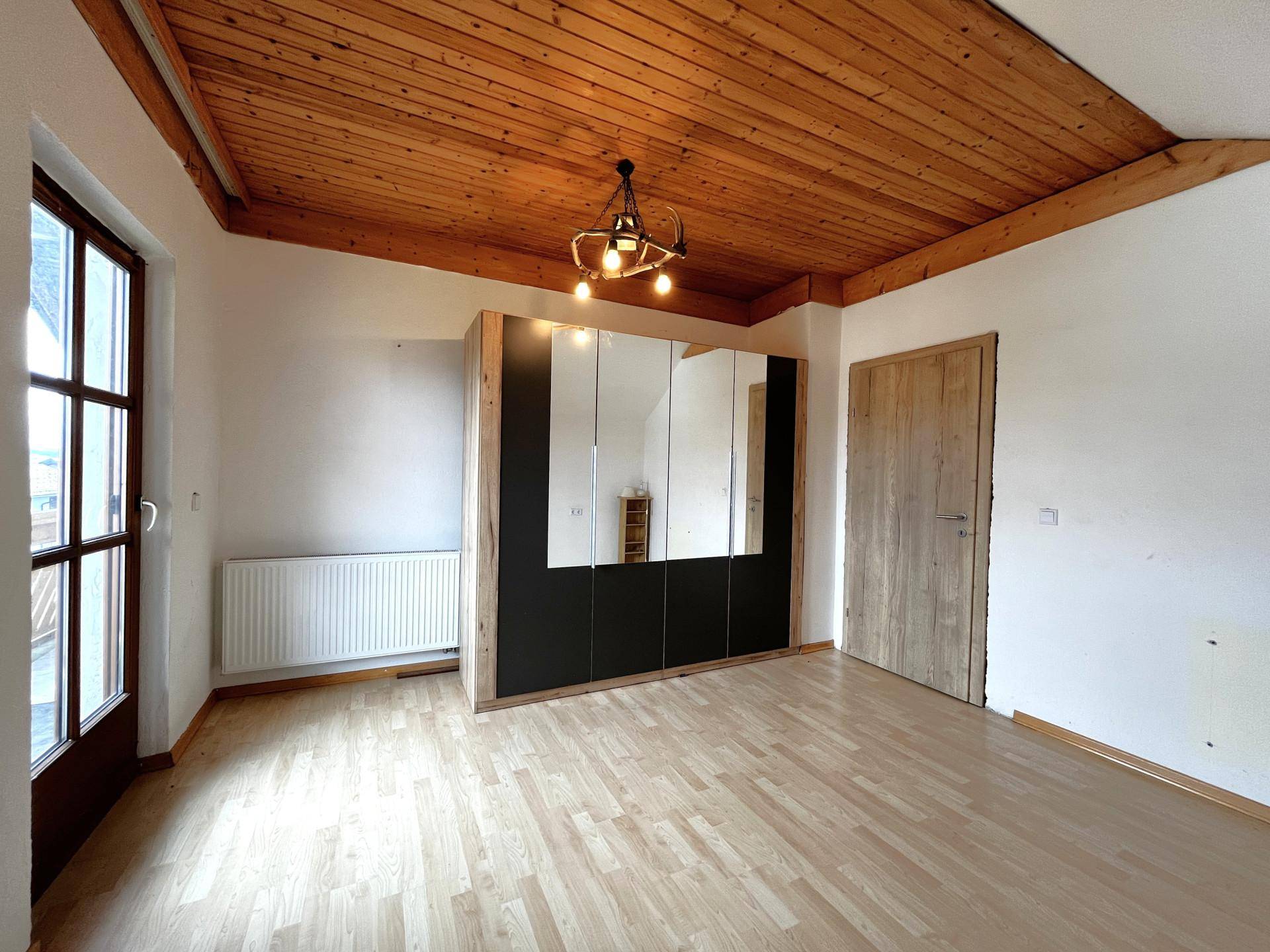 Schlafzimmer mit Holzbalkendecke, Laminatboden und großem Spiegelschrank, hell und einladend.