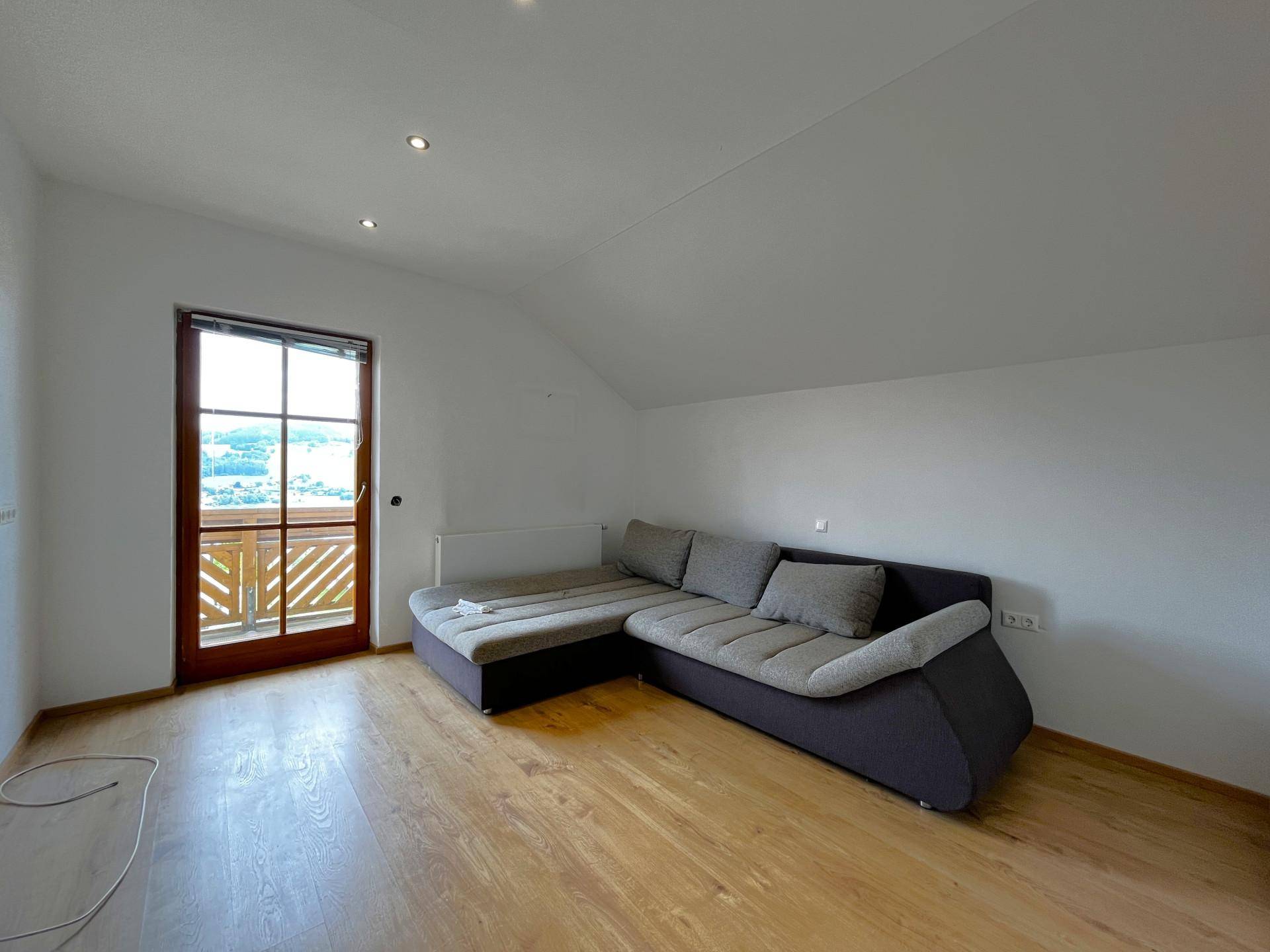Gemütliches Wohnzimmer mit Ecksofa, Holzboden und Zugang zum Balkon unter einer Dachschräge.