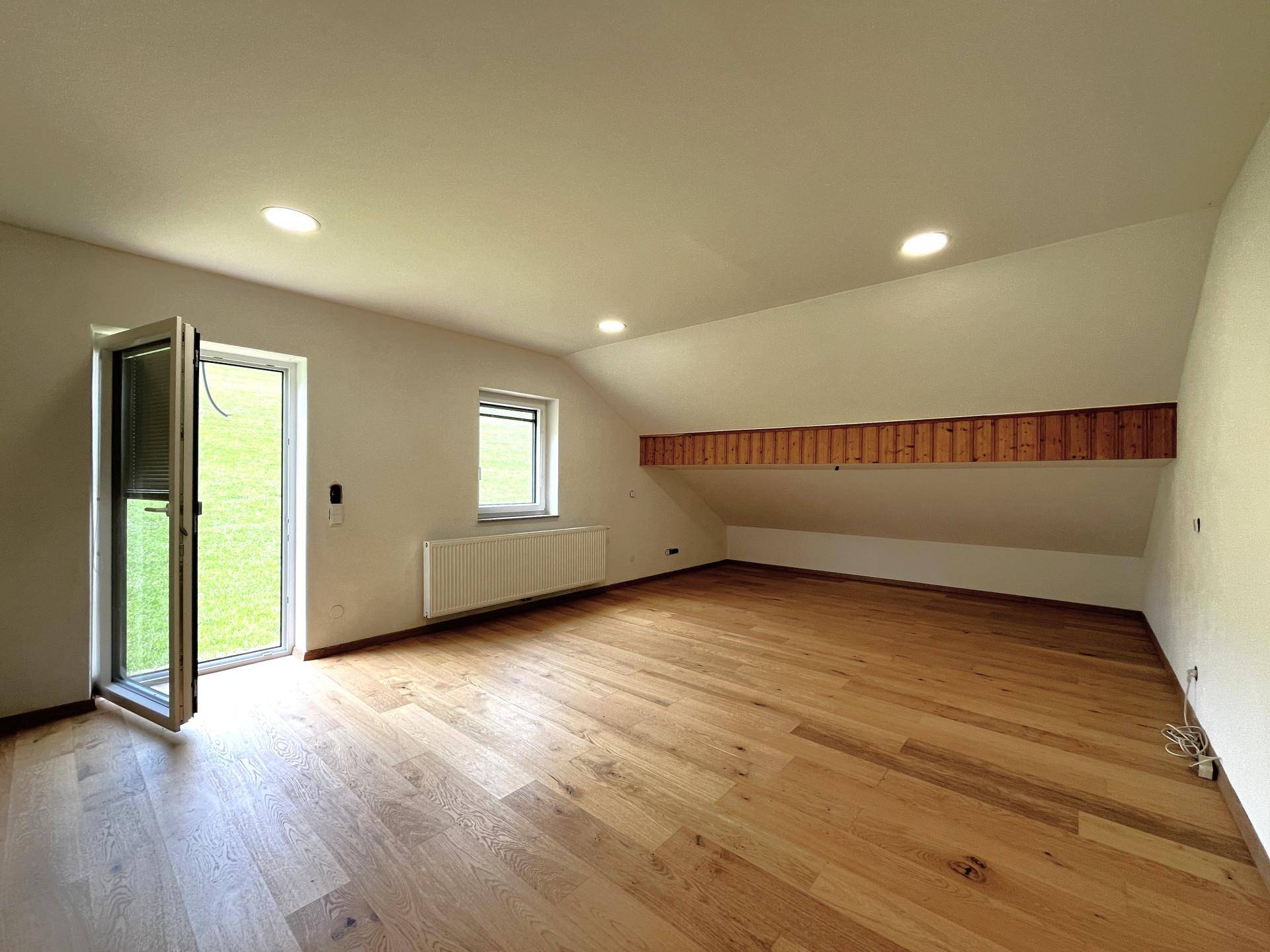 Heller Raum mit Holzboden, Dachschräge und Zugang zum Garten oder Außenbereich.