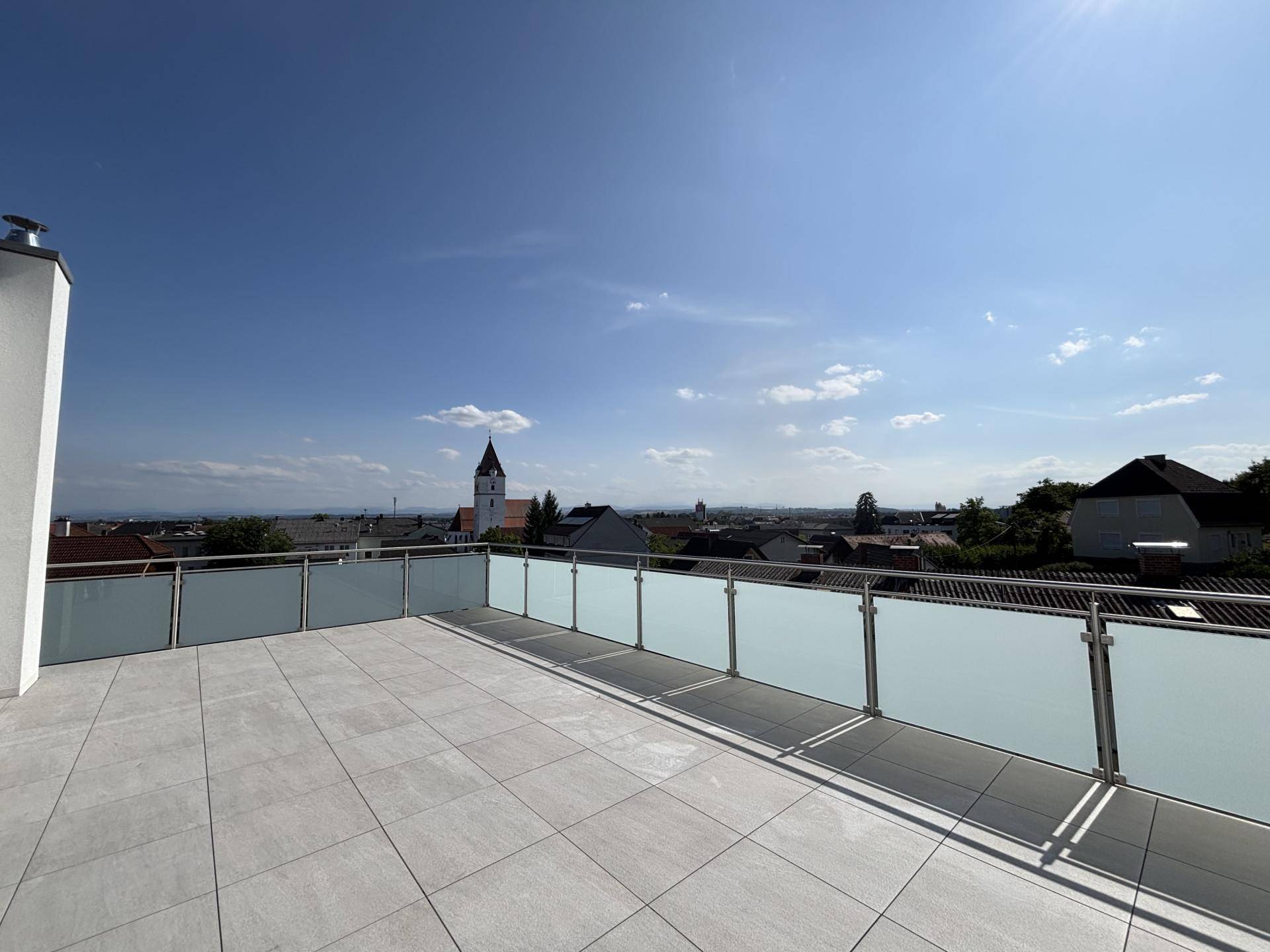 Große Dachterrasse mit Fliesenboden und weitem Blick über die Stadt und Kirchturm.