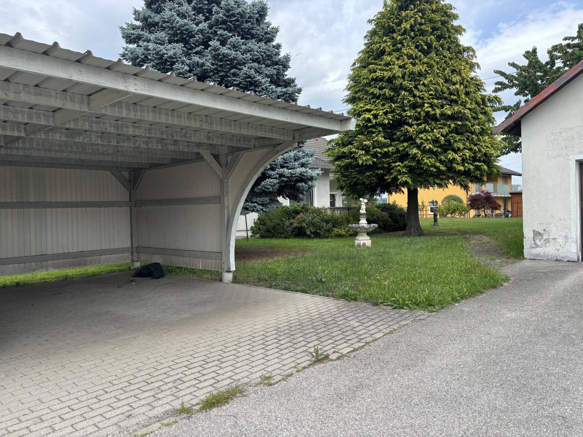 Überdachter Stellplatz (Carport) mit gepflasterter Zufahrt und angrenzendem Gartenbereich.