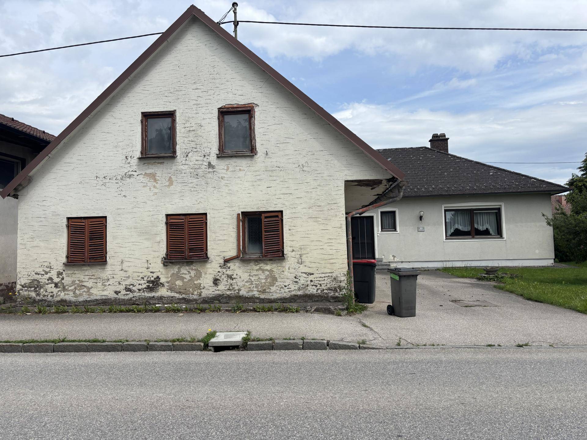 Älterer Gebäudeteil mit abblätternder Fassade und Holzfensterläden an der Straßenseite.