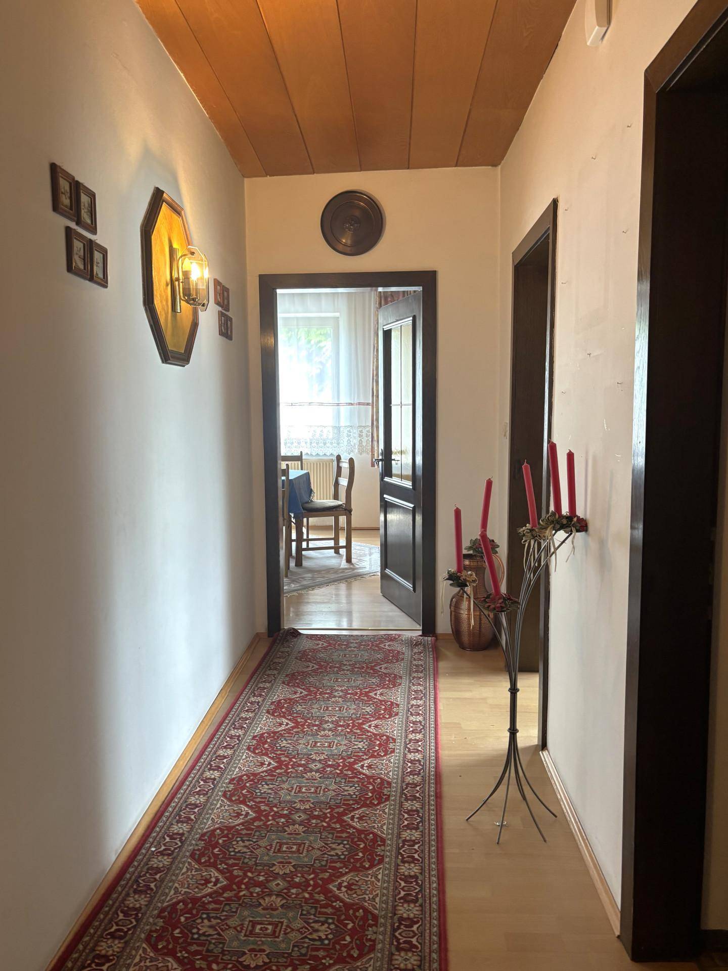 Langer Flur mit gemustertem Teppichläufer, Holzdecke und Zugang zu weiteren Räumen.