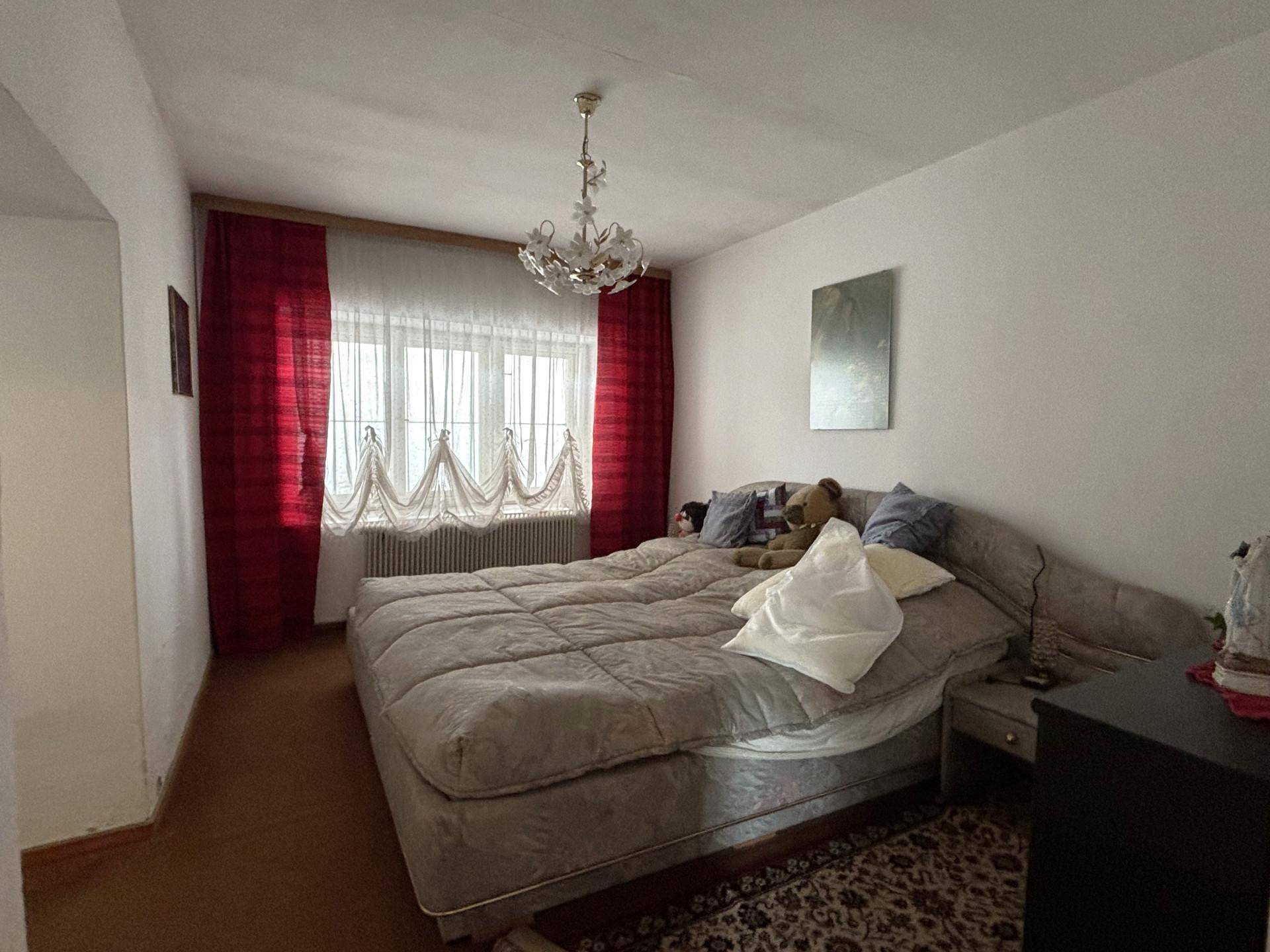 Geräumiges Schlafzimmer mit großem Bett, Teppich und Fenster mit roten Vorhängen.