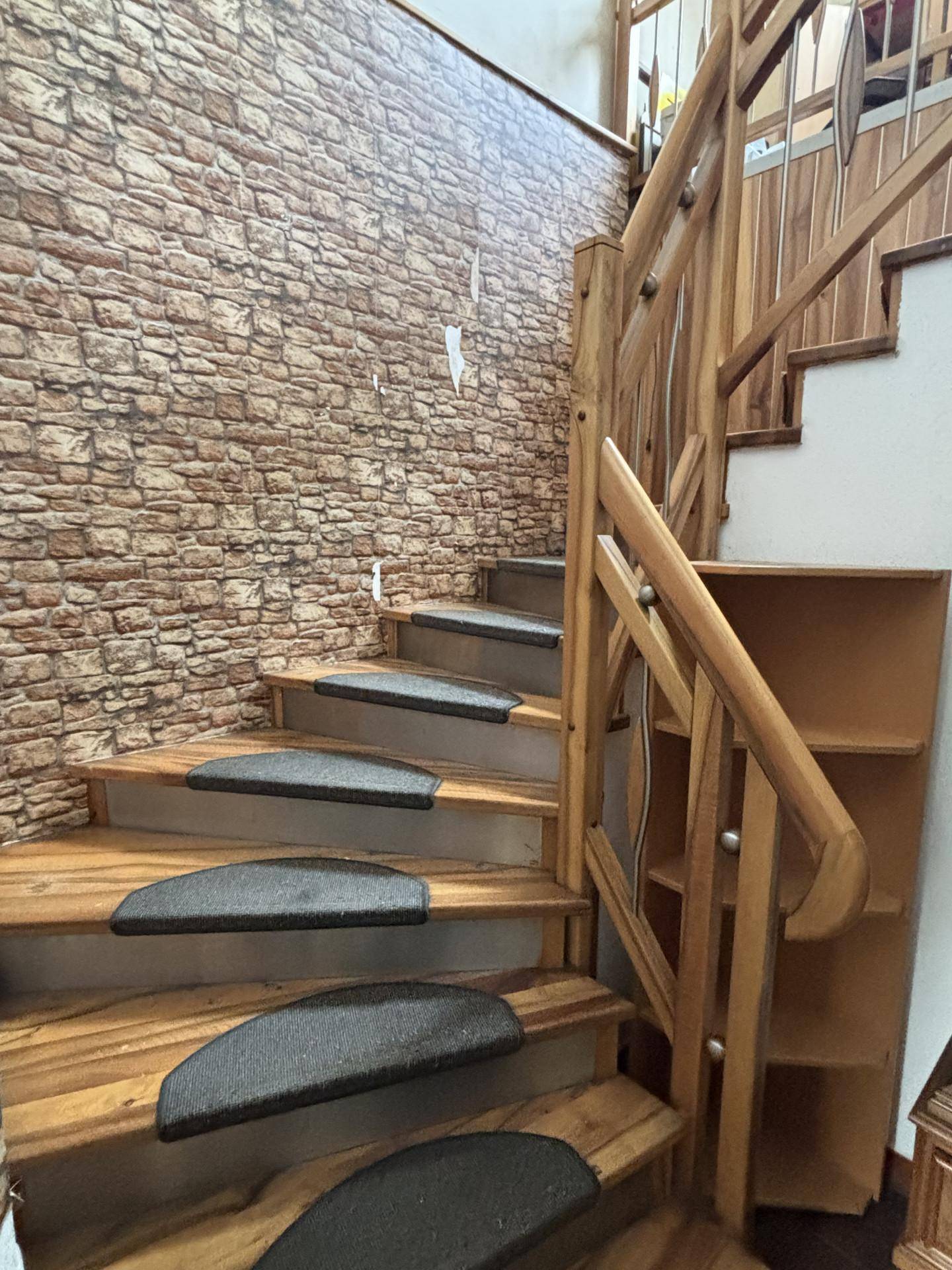 Holztreppe mit gemusterter Tapete und integrierten Regalen, die in ein Obergeschoss führt.