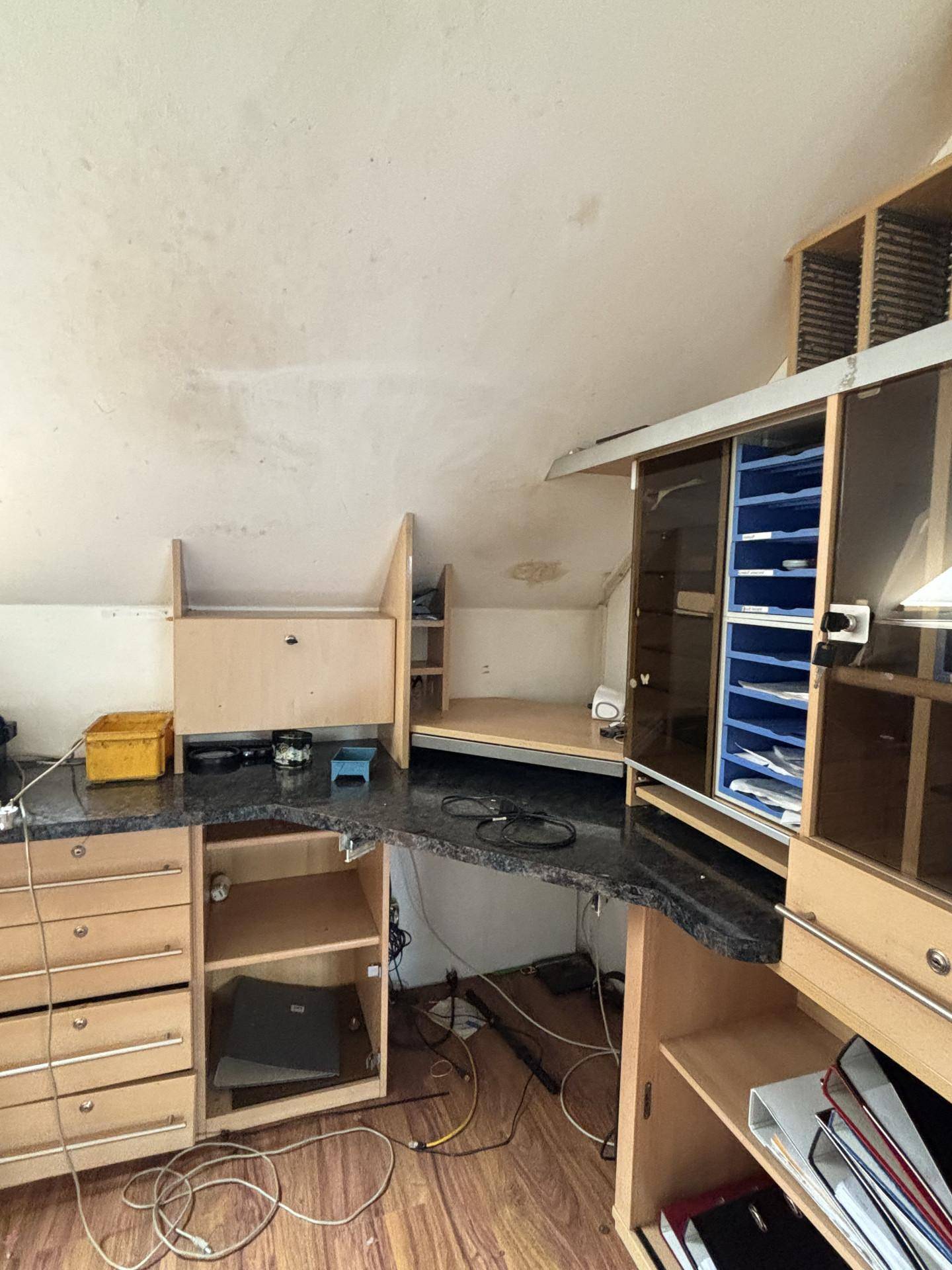 Dachgeschoss-Büro mit Schreibtisch, Regalen und schrägen Wänden unter dem Dach.