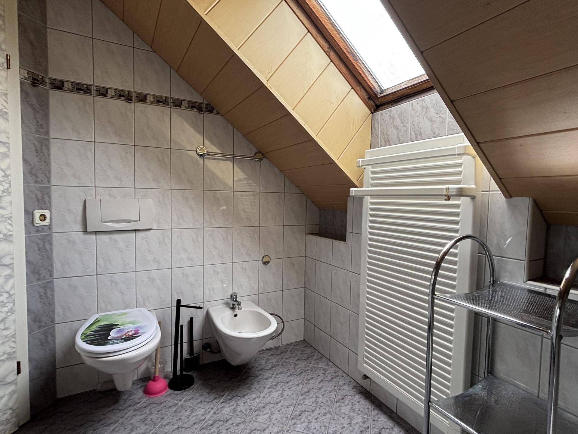 Dachgeschoss-WC mit Bidet, Toilette, Fliesenboden und Dachfenster für natürliches Licht.