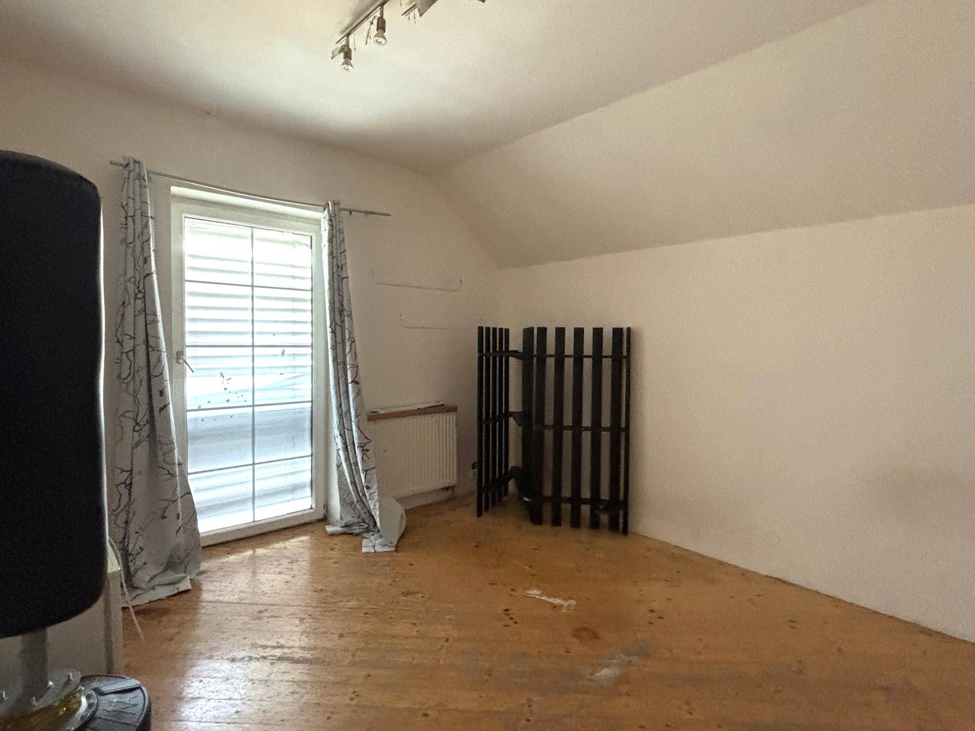 Helles Dachgeschosszimmer mit Holzboden, großem Fenster und schräger Decke.