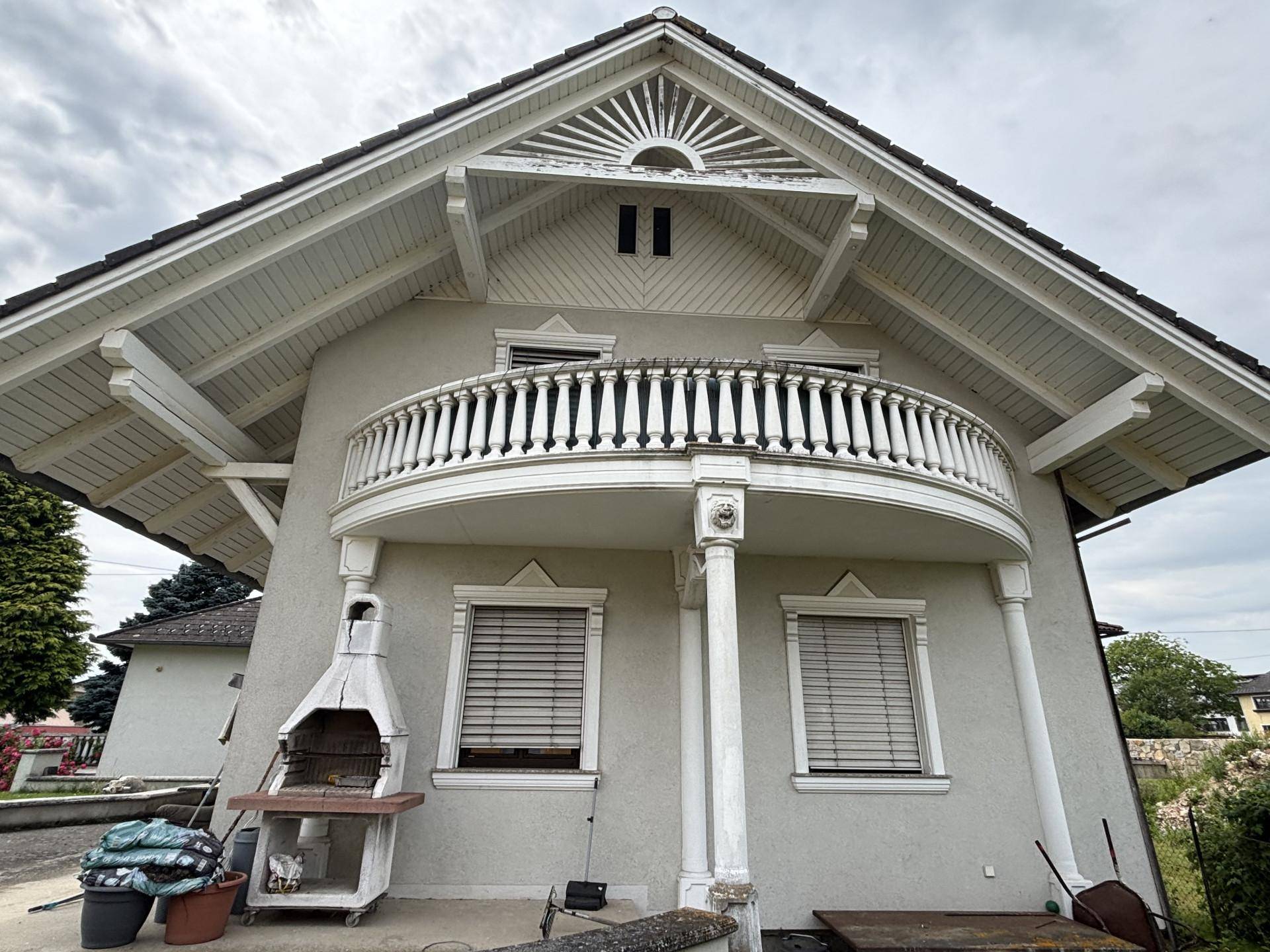 Hausfassade mit einem dekorativen Balkon und einem gemauerten Grill im Außenbereich.
