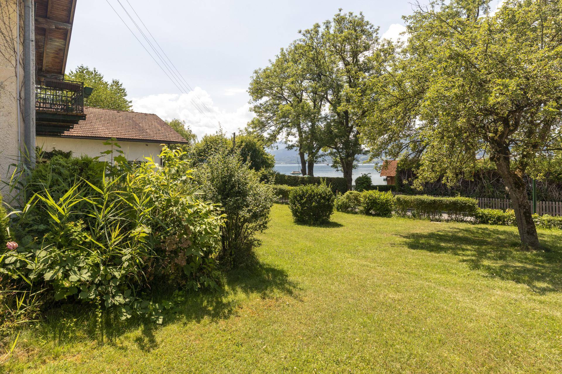 Großer, sonniger Gartenbereich mit Rasenfläche und Blick auf den See im Hintergrund.