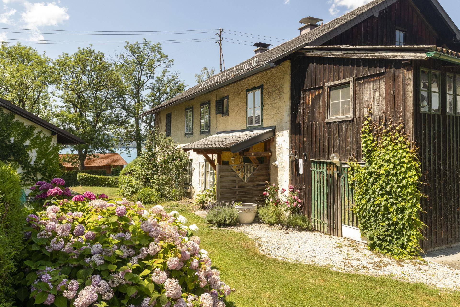 Seitenansicht des Hauses mit blühenden Hortensien und einem charmanten Garten mit Seeblick.
