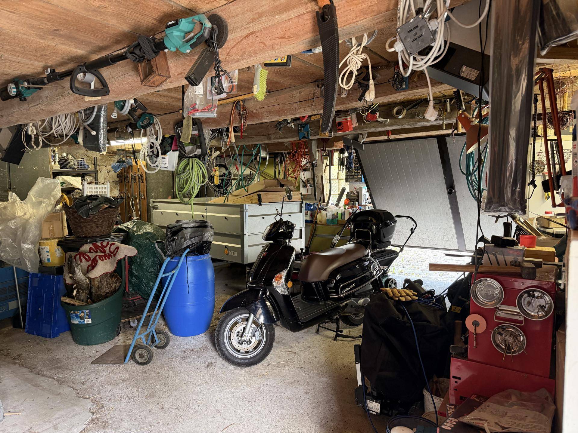 Geräumige Garage mit Motorroller, Anhänger und diversen Werkzeugen und Geräten.