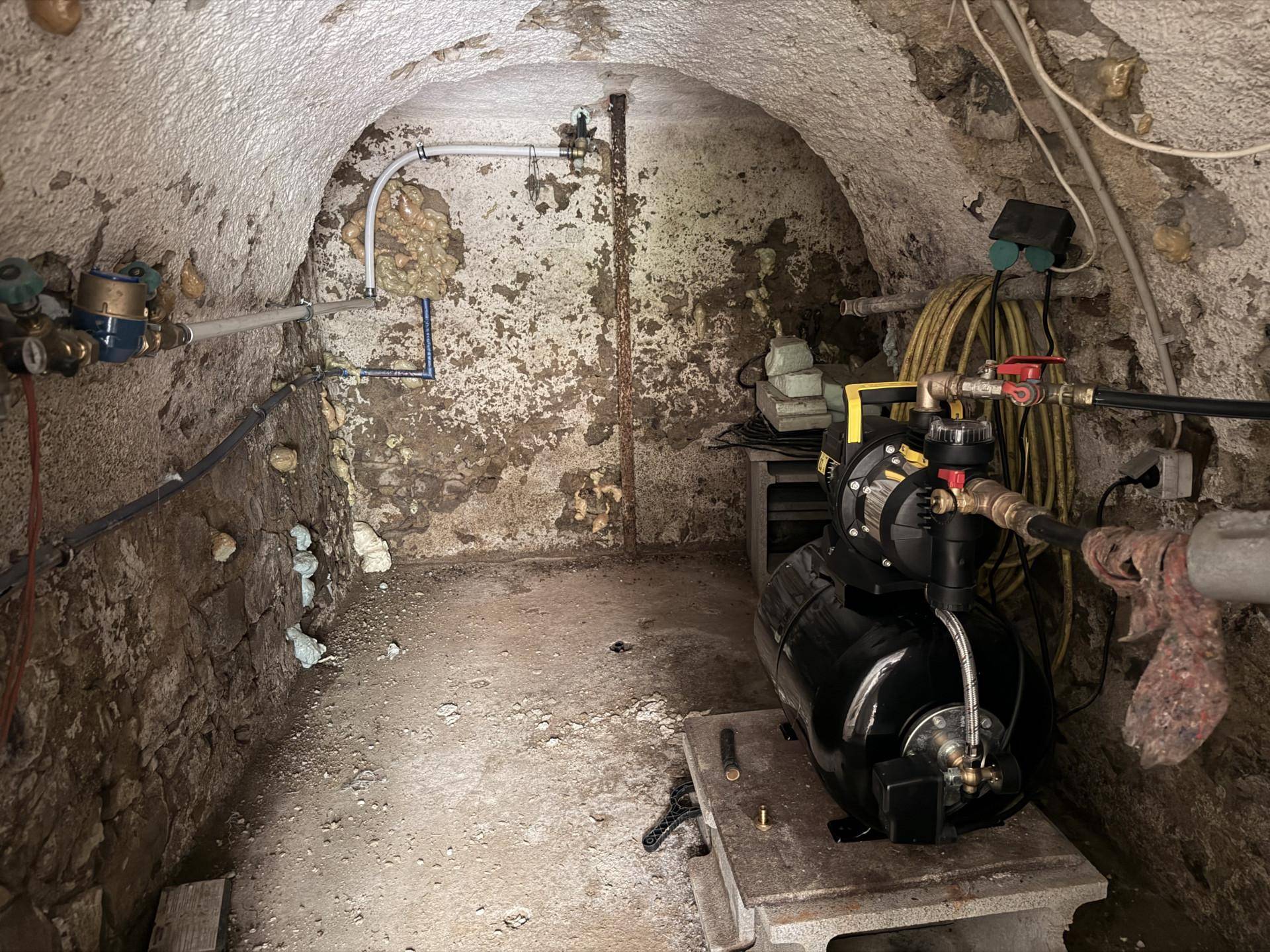Technikraum im Keller mit Wasserleitungen und Pumpenanlage.