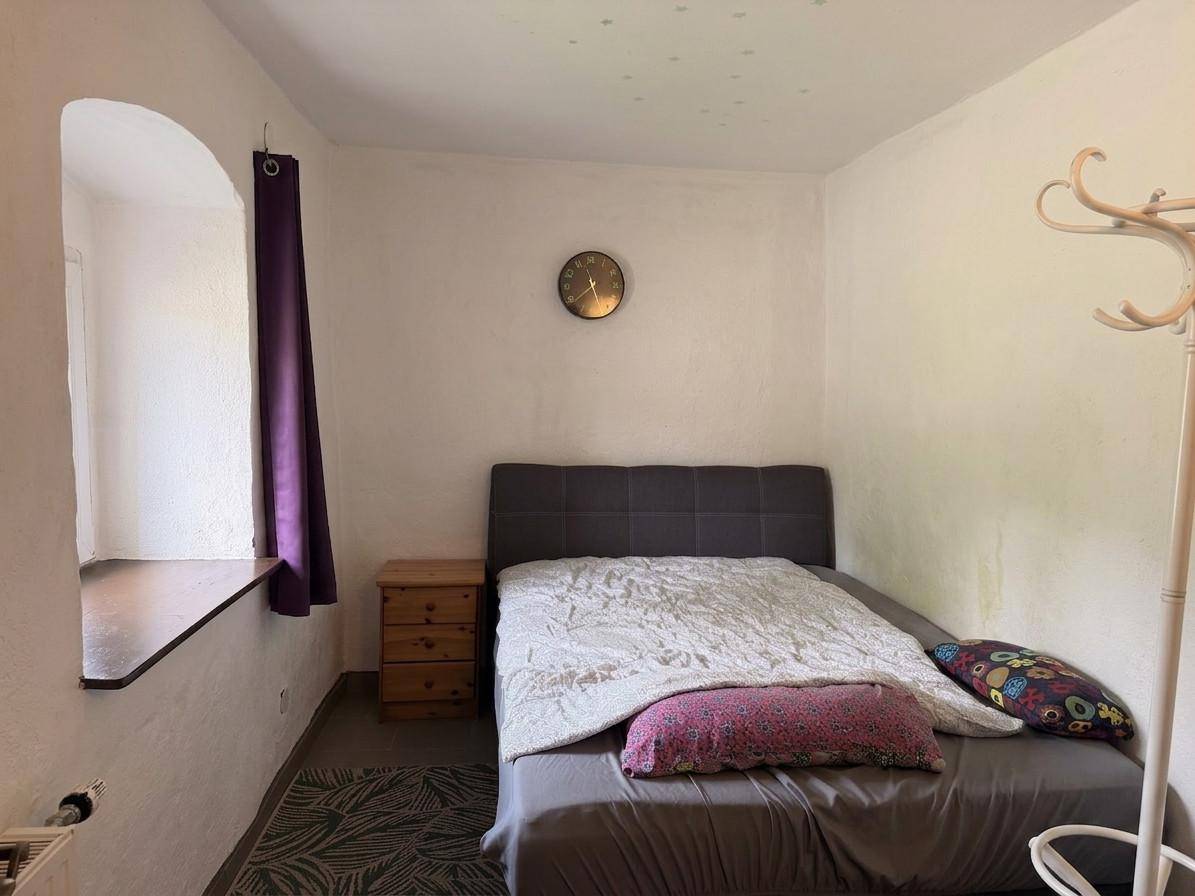 Schlafzimmer mit Einzelbett, Nachttisch und einem Fenster mit tiefer Laibung.
