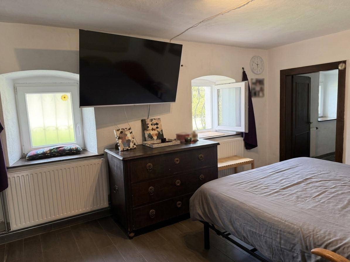 Schlafzimmer mit Fernseher, Kommode und zwei Fenstern für natürliches Licht.