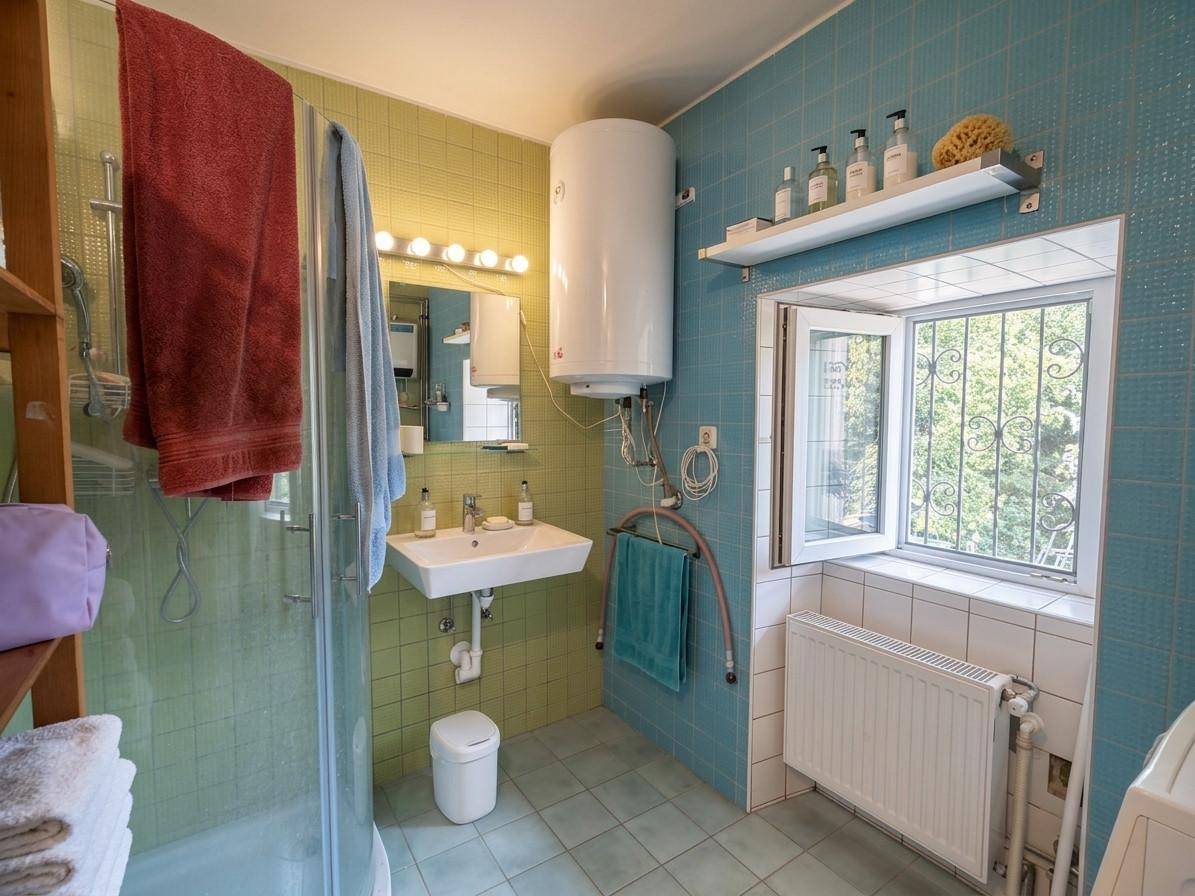 Badezimmer mit Dusche, Waschbecken und farbigen Fliesen in Blau- und Grüntönen.