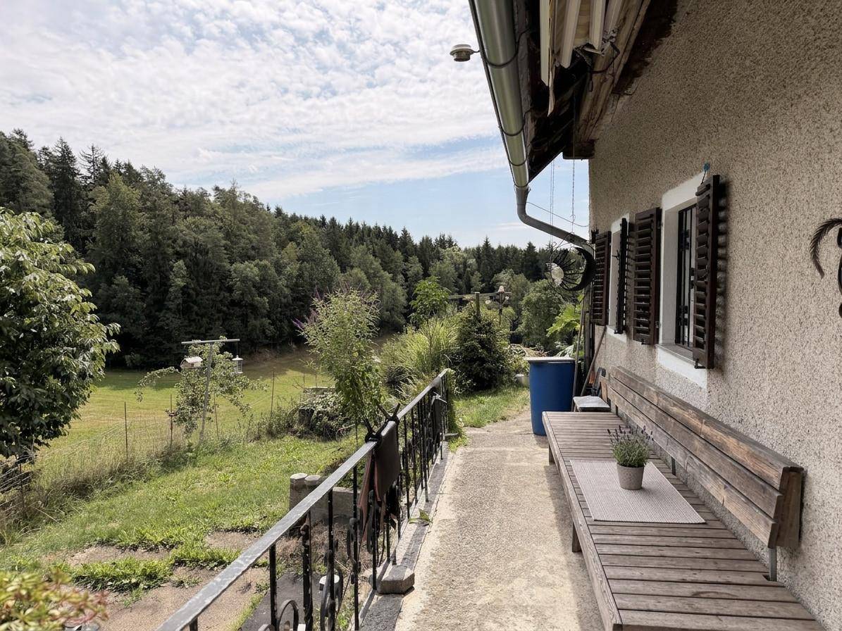 Schmale Terrasse mit Holzsitzbank und weitem Blick über grüne Felder und Wälder.