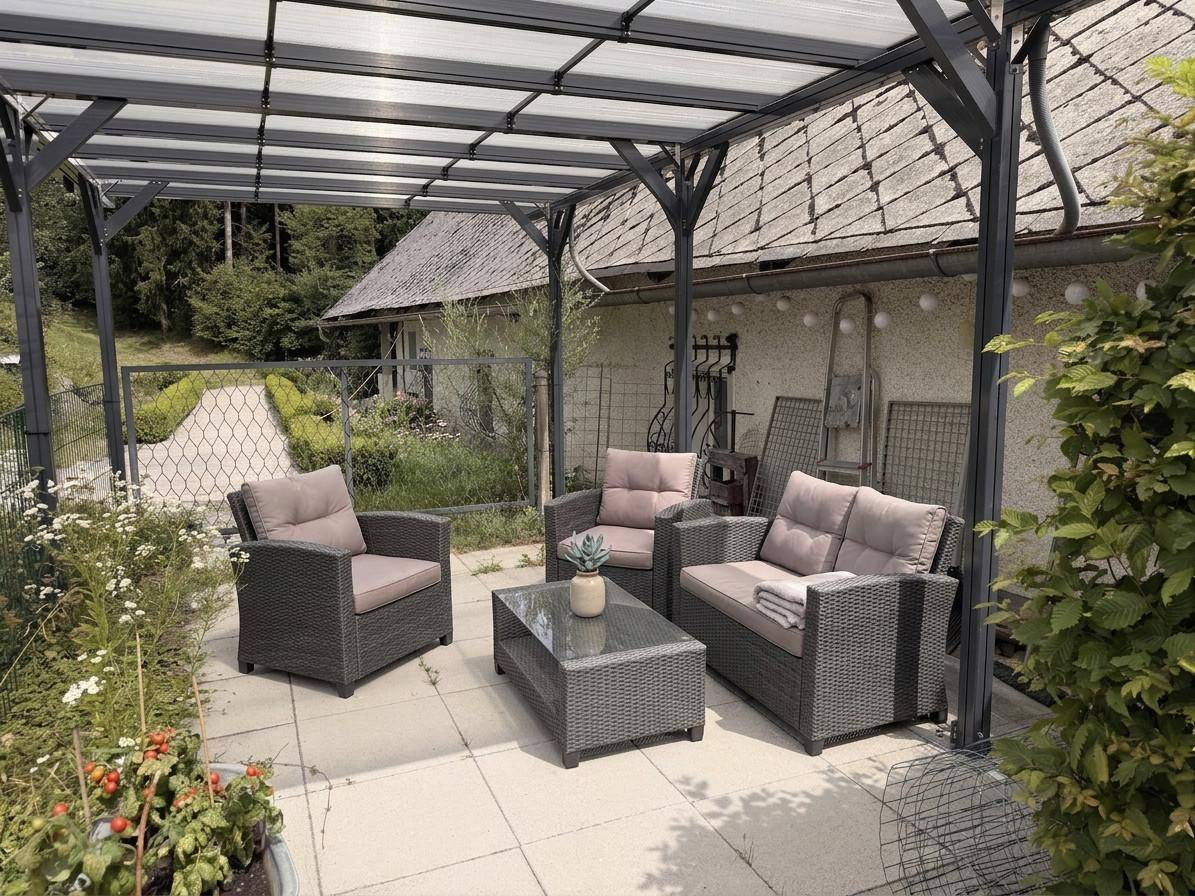 Überdachte Terrasse mit bequemen Gartenmöbeln und Blick auf das Haus.