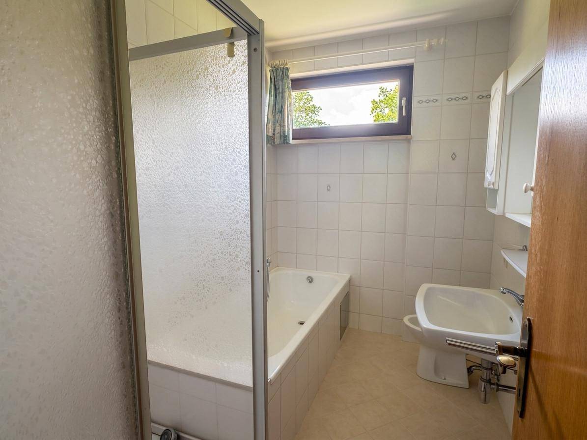 Badezimmer mit Badewanne, Duschabtrennung, Waschbecken und Fenster.