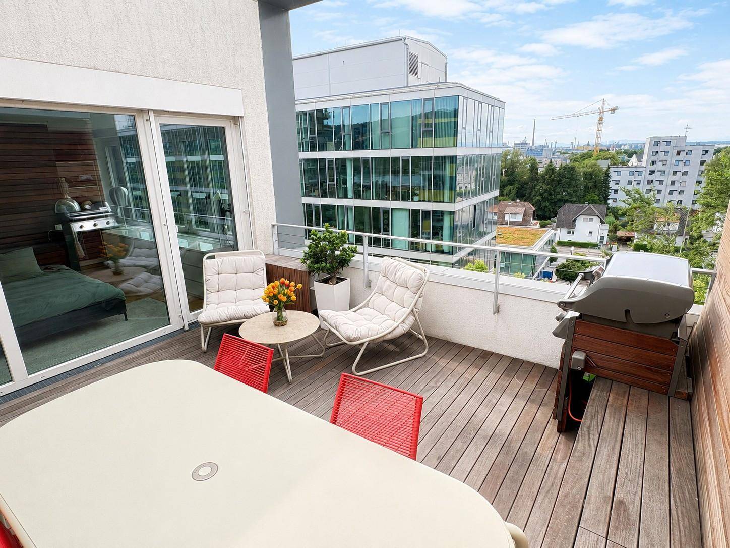 Geräumige Terrasse mit Holzboden, Gartenmöbeln und Grillbereich, bietet einen weiten Blick über die Stadt.