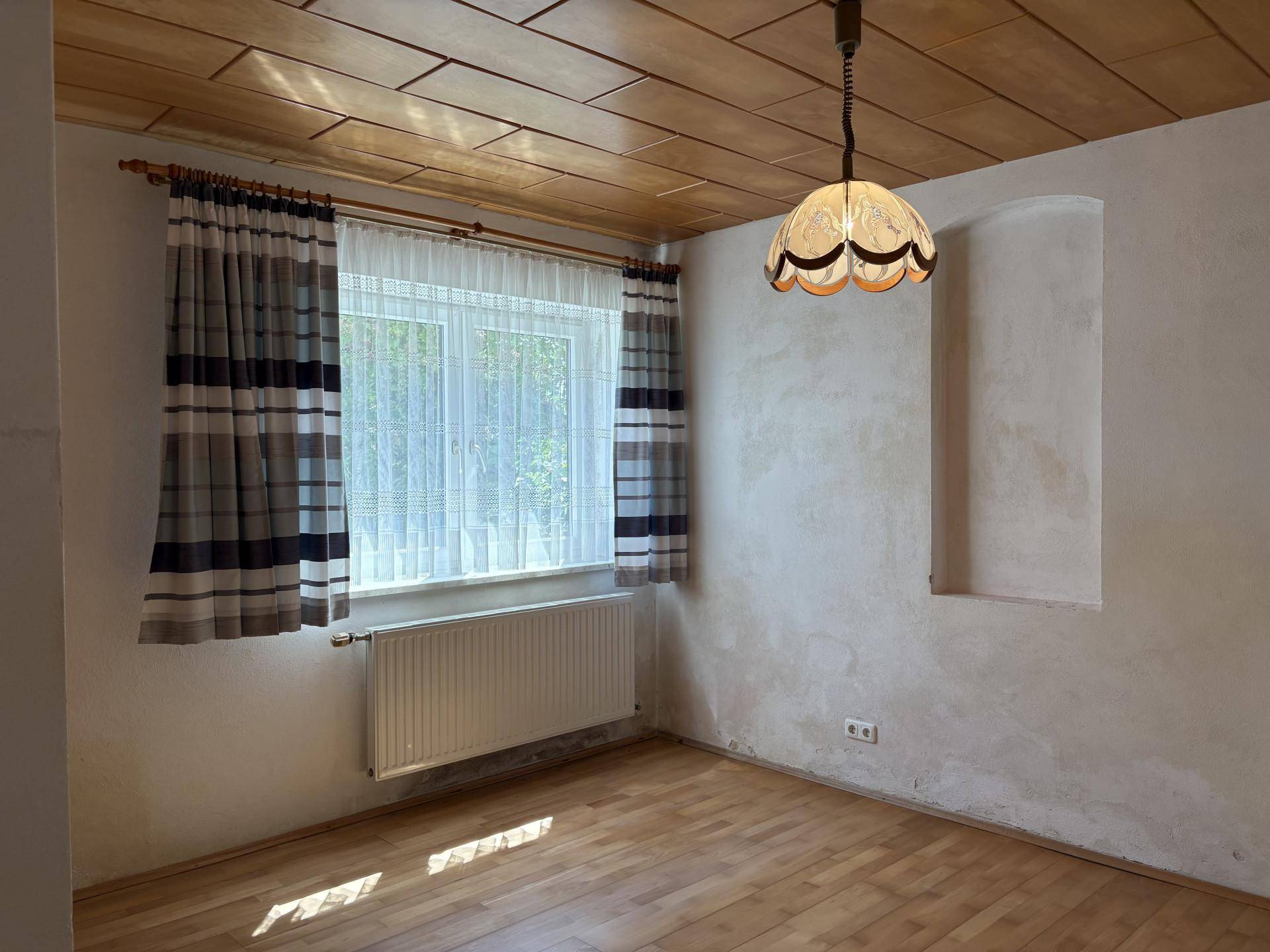 Leerer Raum mit Holzdecke, Parkettboden und einem Fenster, das viel Tageslicht hereinlässt.