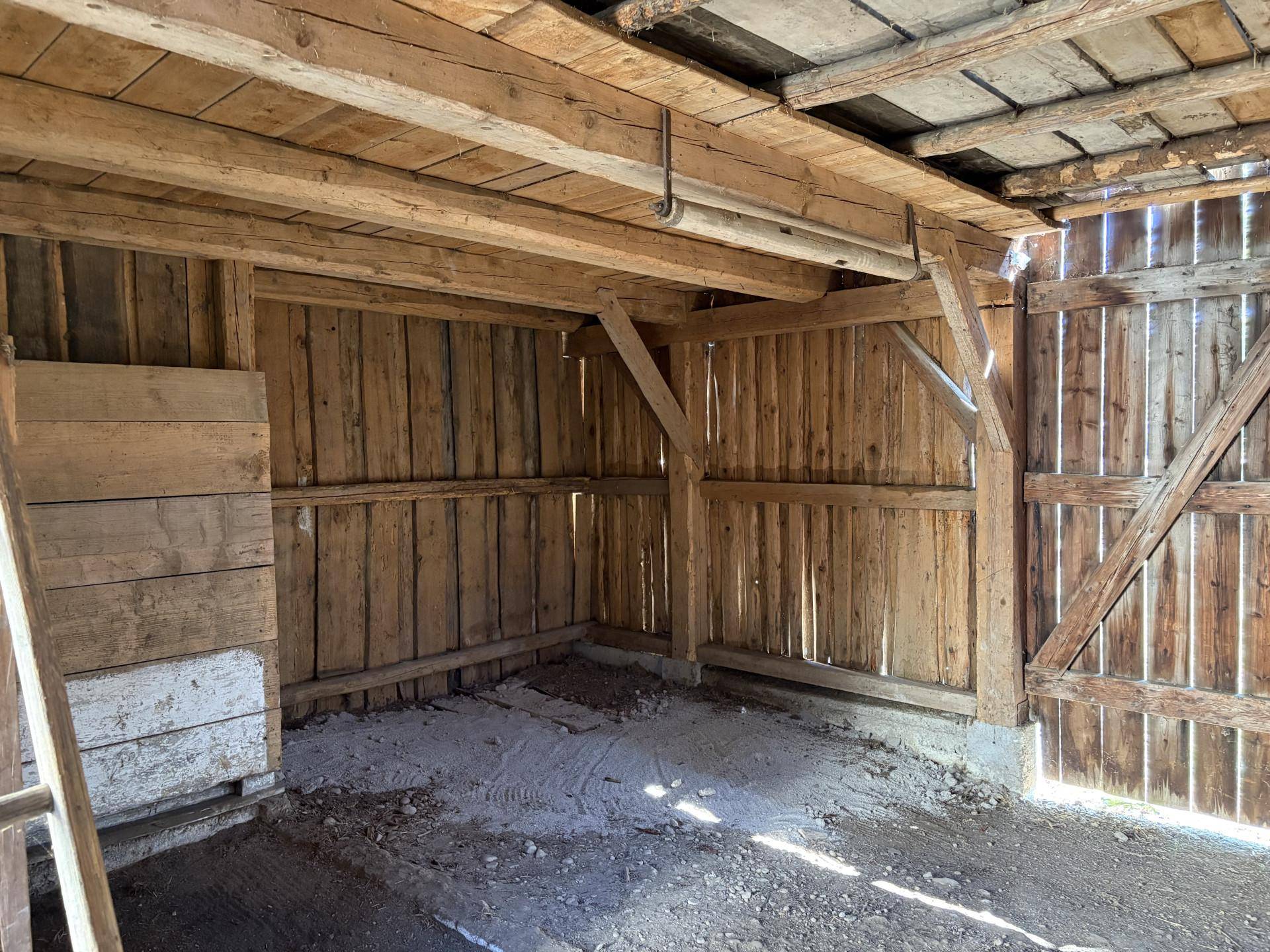 Innenansicht einer Holzscheune mit sichtbaren Balken und einfacher Holzverkleidung.