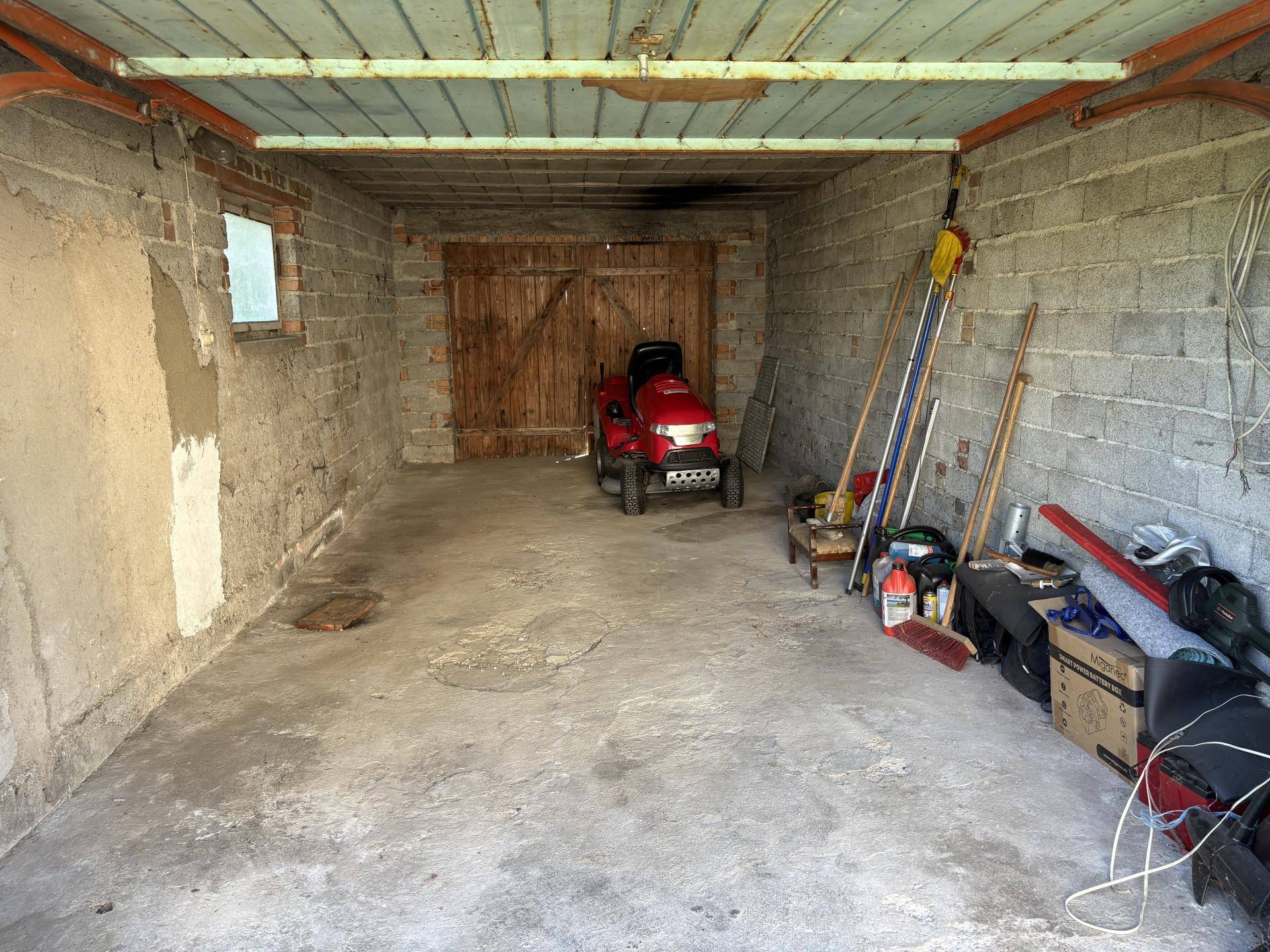 Geräumige Garage mit Betonwänden und -boden, genutzt als Abstellraum für Gartengeräte.