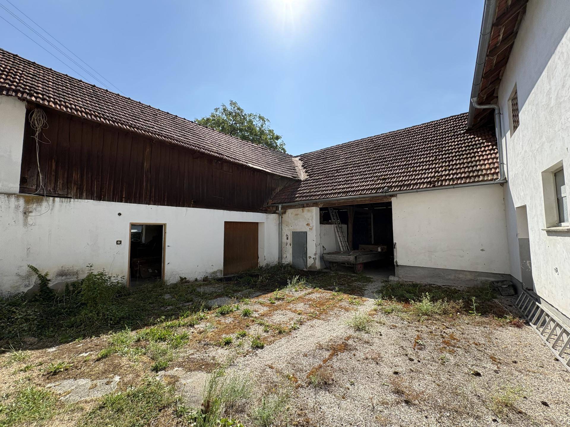 Alter Bauernhof mit großem Innenhof und Nebengebäuden unter strahlend blauem Himmel.