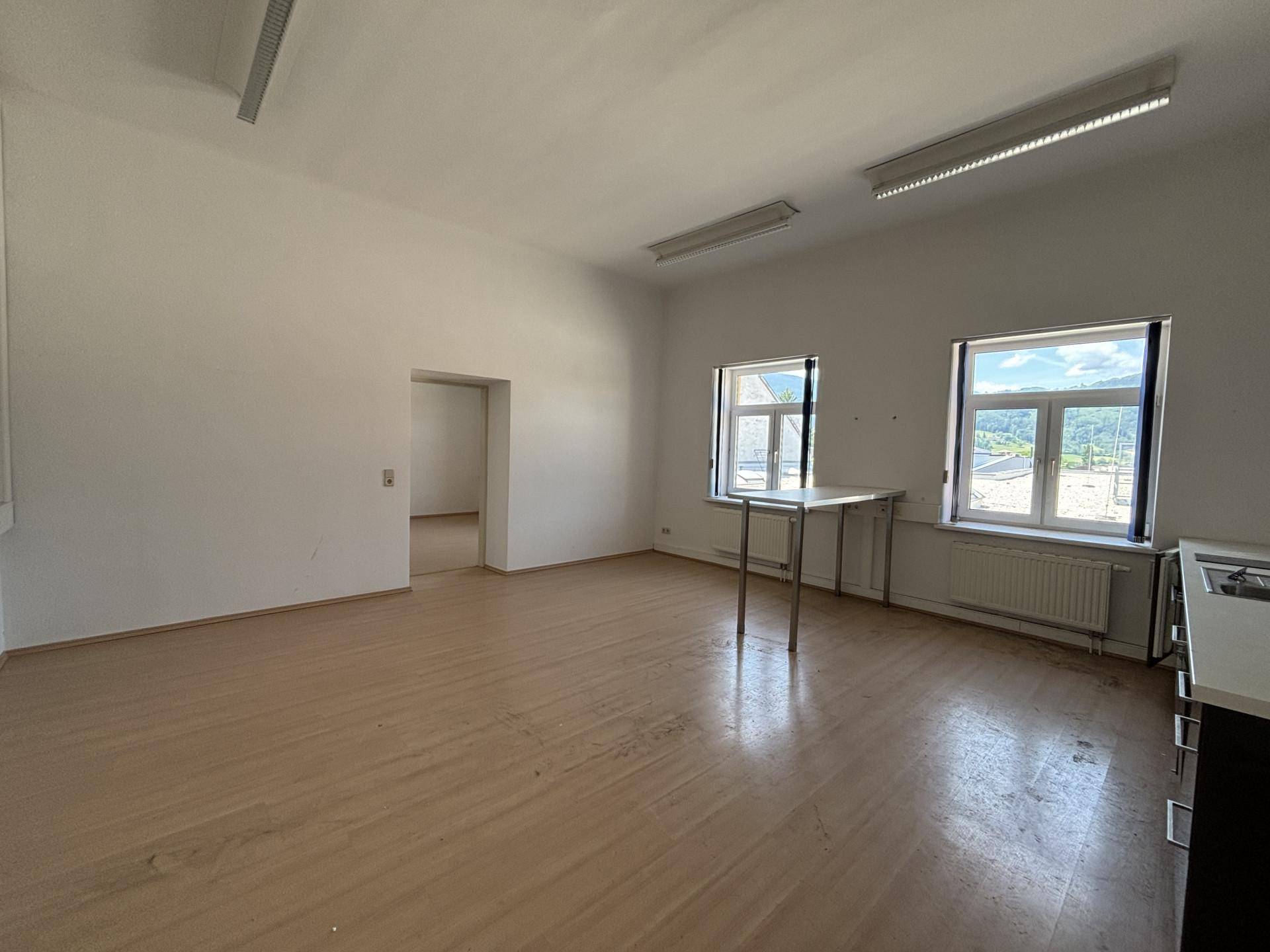 Großer, heller Raum mit Holzboden und Fenstern, die einen Blick auf die Umgebung bieten, ideal für Bürozwecke.