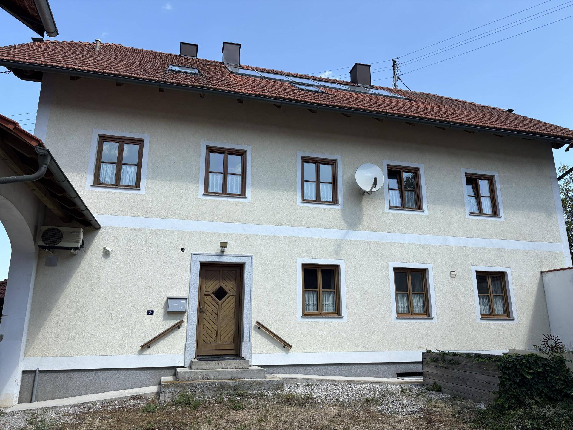 Vorderansicht des Hauses mit mehreren Fenstern, Satellitenschüssel und traditionellem Dach.