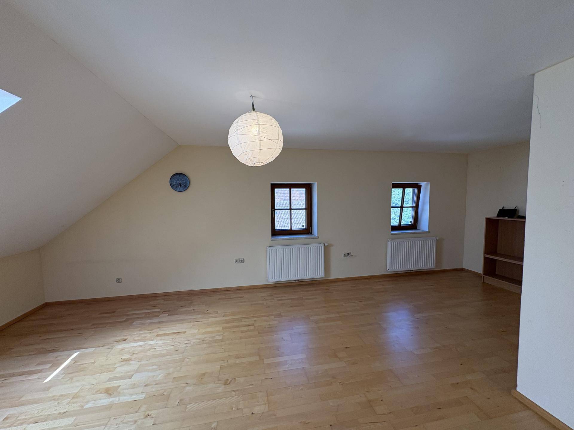 Helles Dachzimmer mit schrägen Wänden, Holzboden und zwei Fenstern für natürliches Licht.