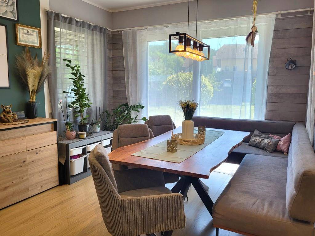Gemütlicher Essbereich mit Holztisch, Sitzbank und großen Fenstern mit Blick ins Grüne.