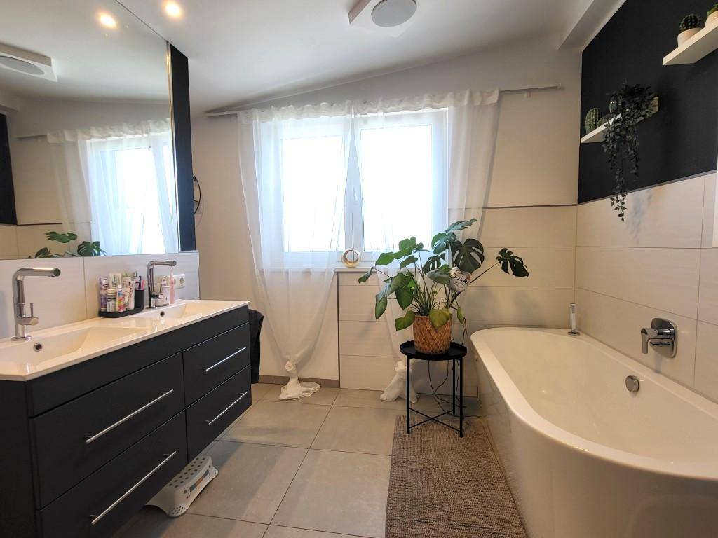 Helles Badezimmer mit Doppelwaschbecken, Badewanne und großem Spiegel.
