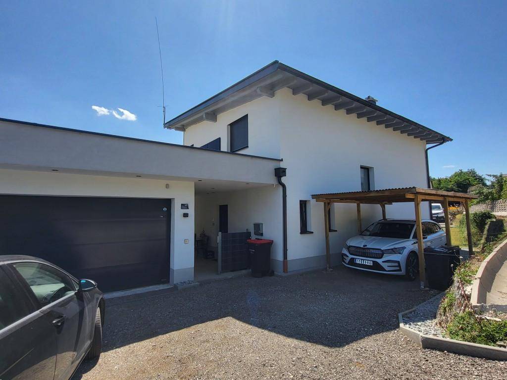 Modernes Einfamilienhaus mit Doppelgarage, Carport und gepflasterter Auffahrt.