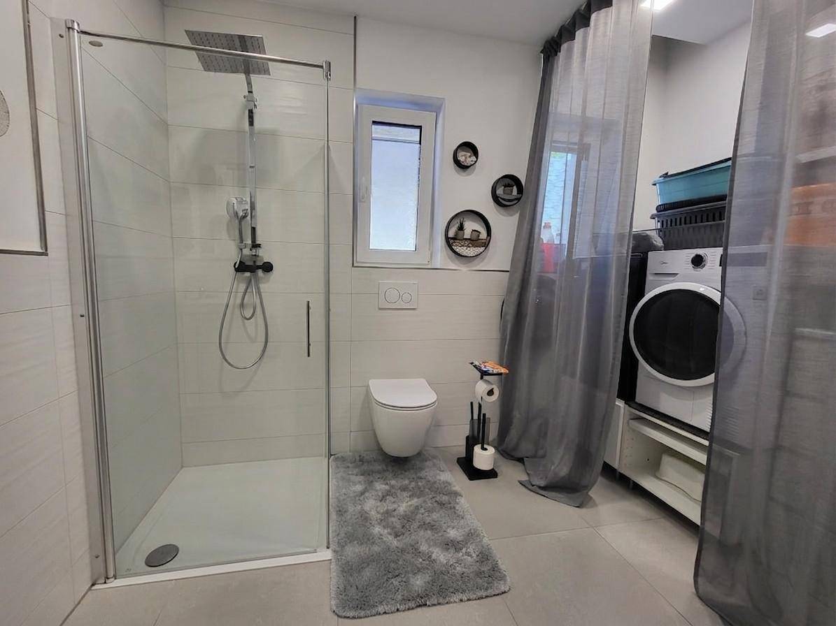 Modernes Badezimmer mit ebenerdiger Dusche, WC und Waschmaschine.